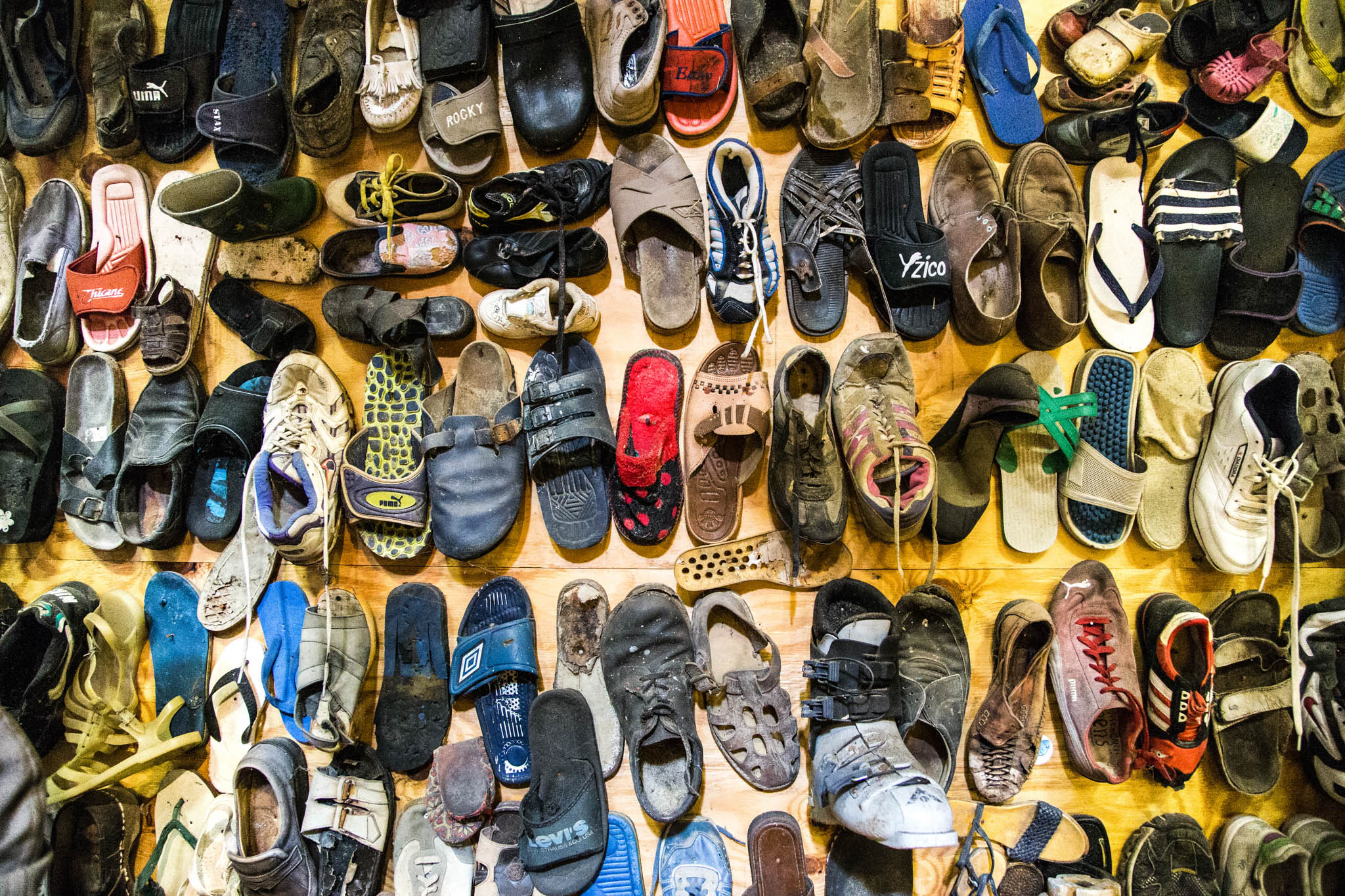 Collection of diverse, well-worn footwear displayed on a wall, including sneakers, sandals, and boots in vibrant colors.