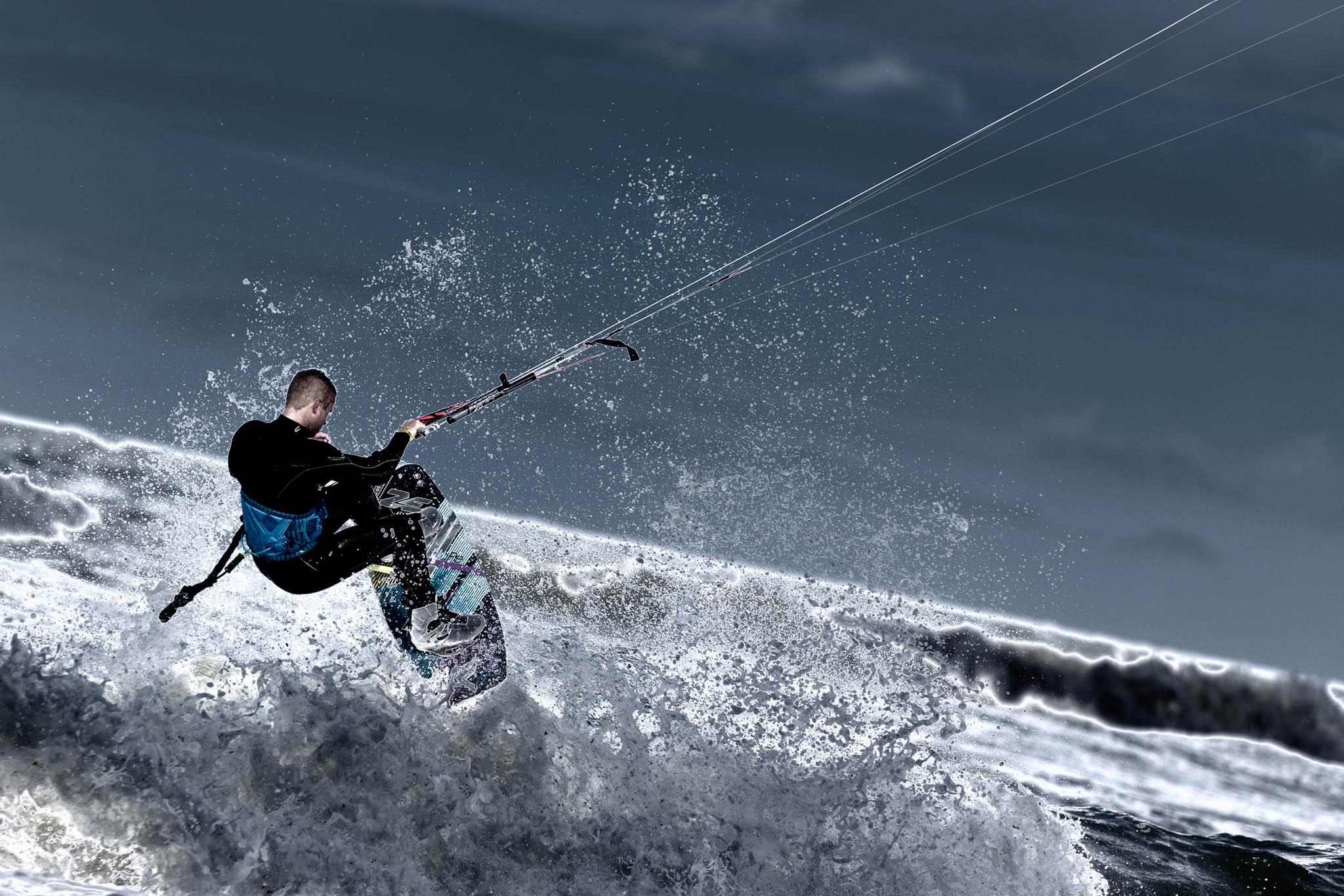 Kitesurfer performing a high jump over ocean waves on a windy day, with dramatic water spray and dark sky.