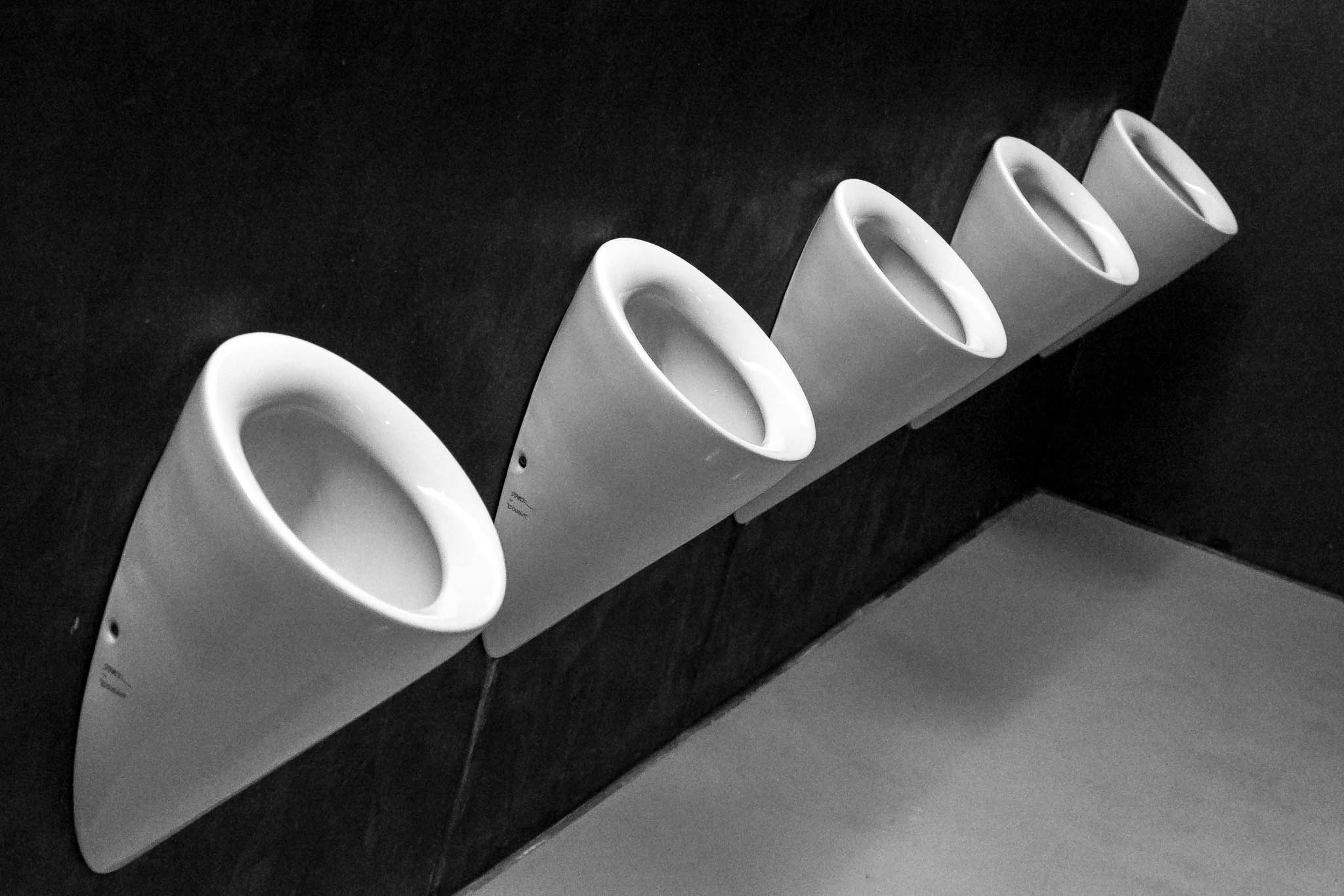 Row of modern white urinals on dark wall in public restroom.