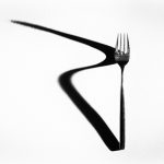 Fork casting a long zigzag shadow on a white surface, creating a striking minimalist composition.