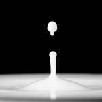 Milk droplet splashes into a smooth surface creating a crown effect against a black background.