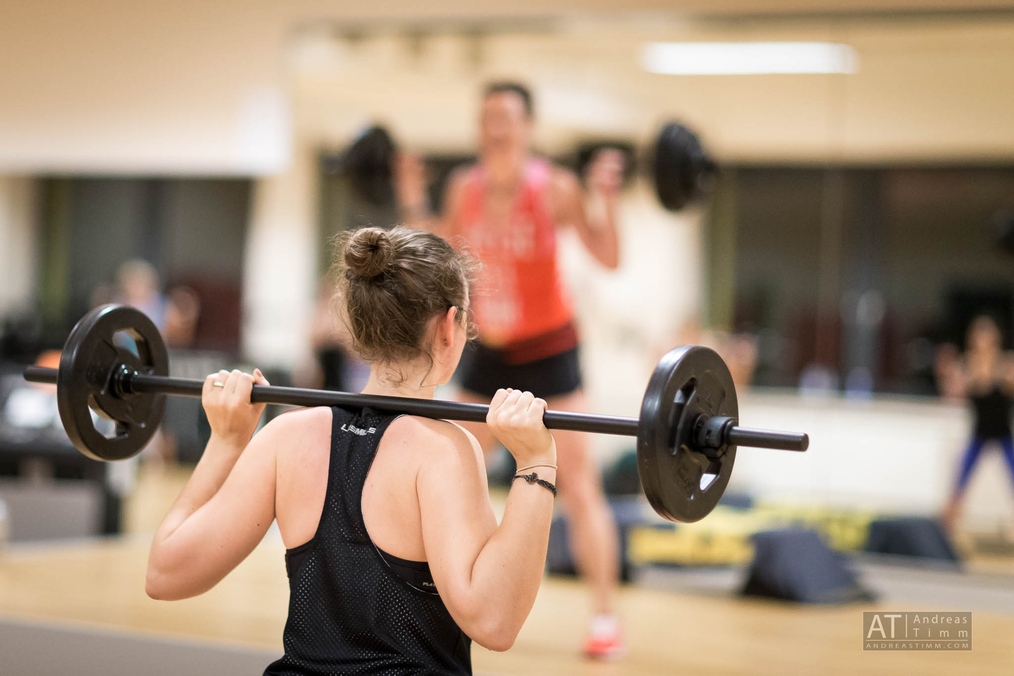 Person lifting a barbell in a fitness class, focusing on strength training in a gym setting.