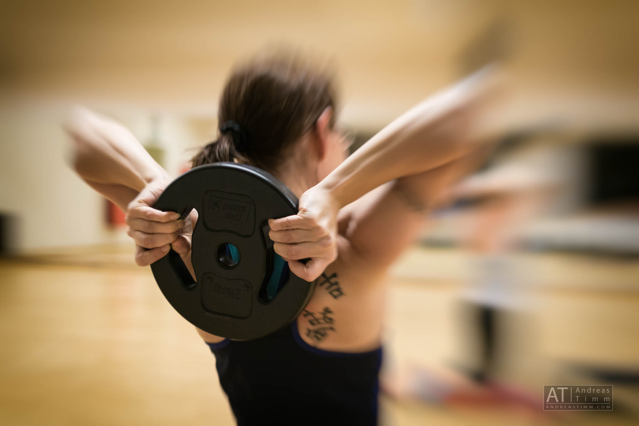 Person lifting a weight plate overhead in a gym, focusing on upper body strength training.