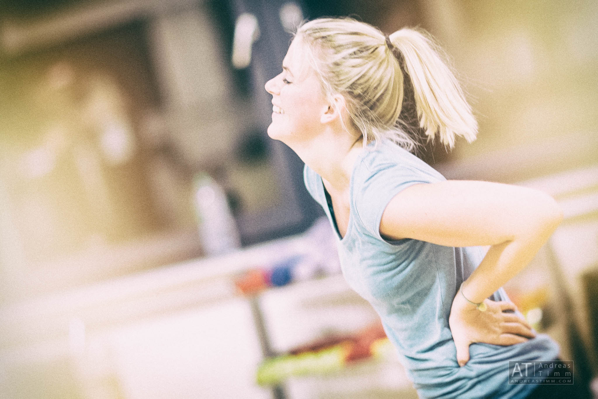 Smiling woman in a blue shirt with hands on hips, enjoying exercise in a bright indoor setting.