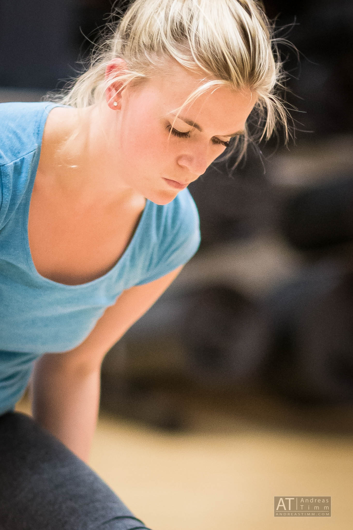 Person focused in a workout, wearing a blue shirt, blonde hair tied back, exercising indoors.