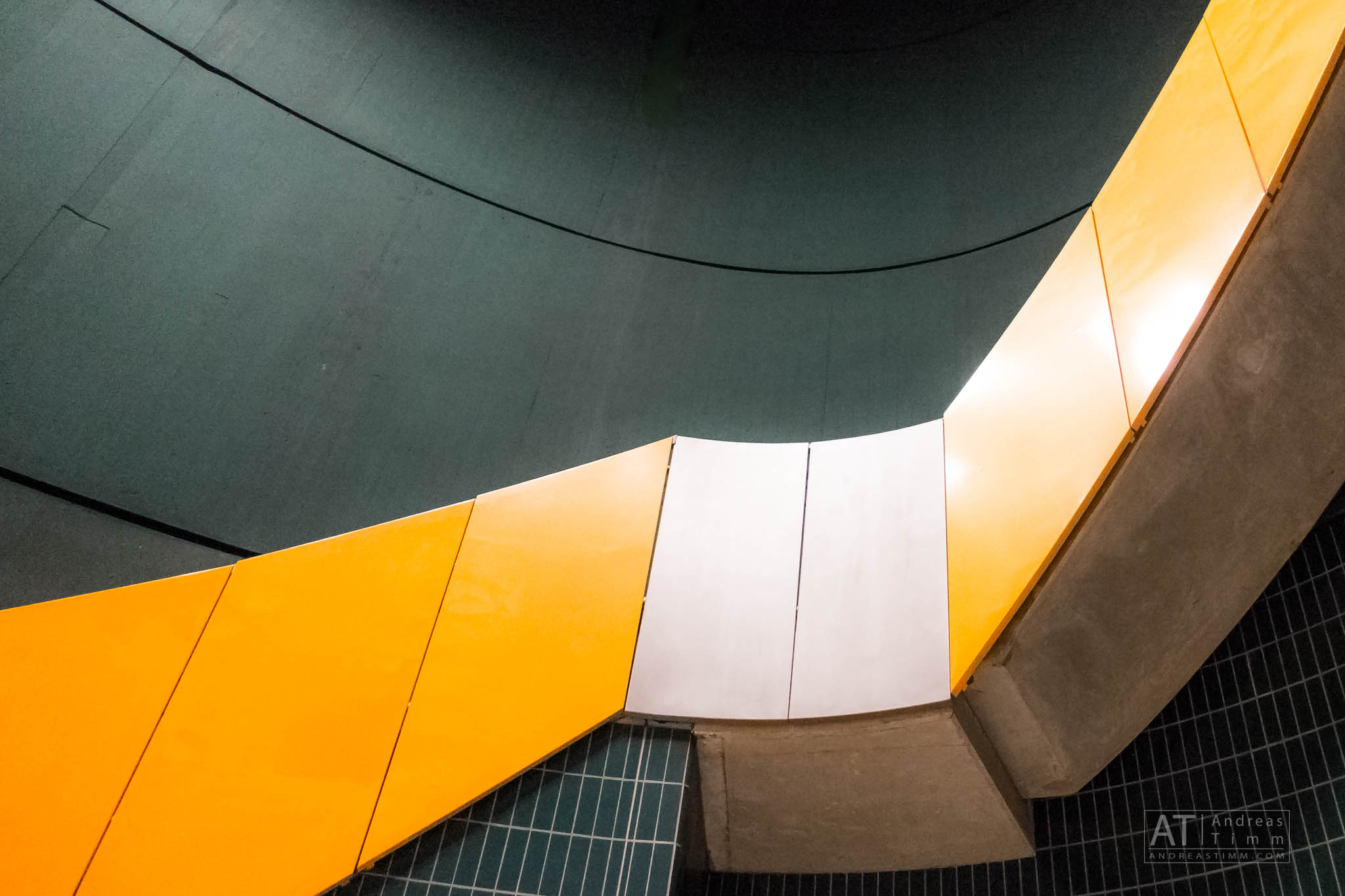 Curved wall with yellow and white panels and a dark teal background in modern architectural design.
