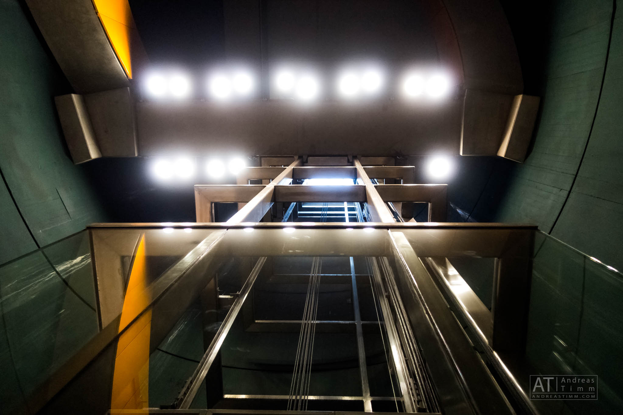 Looking up the inside of a brightly lit elevator shaft with metal beams and cables.