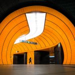 Modern metro station with bright orange curved walls and a silhouette of a person walking, sign pointing to Odeonsplatz.