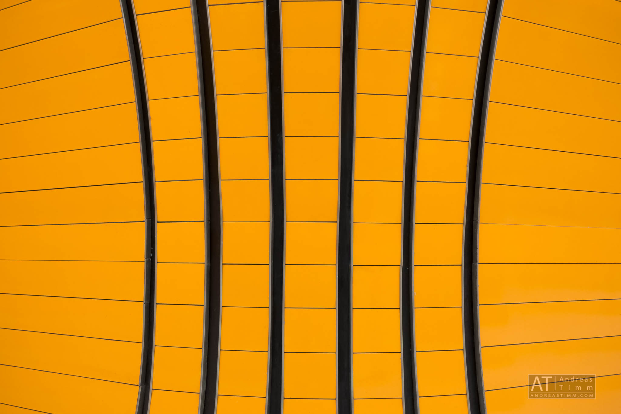 Curved orange structure with vertical black lines creating an abstract geometric pattern.