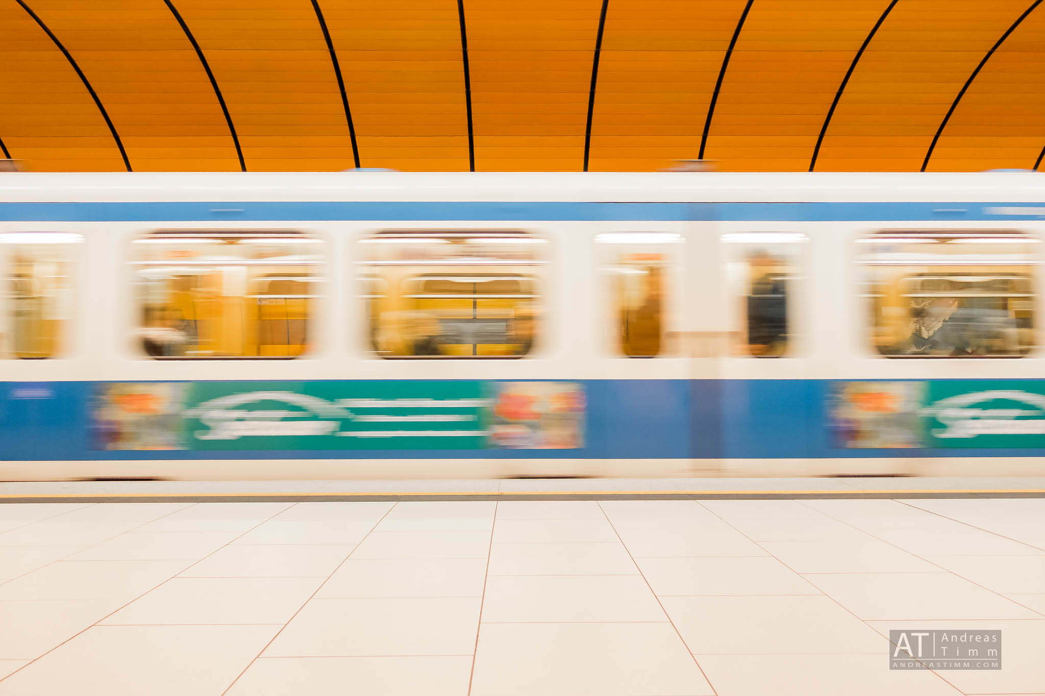 Blurred blue and white subway train speeds by in a station with orange arched ceiling.