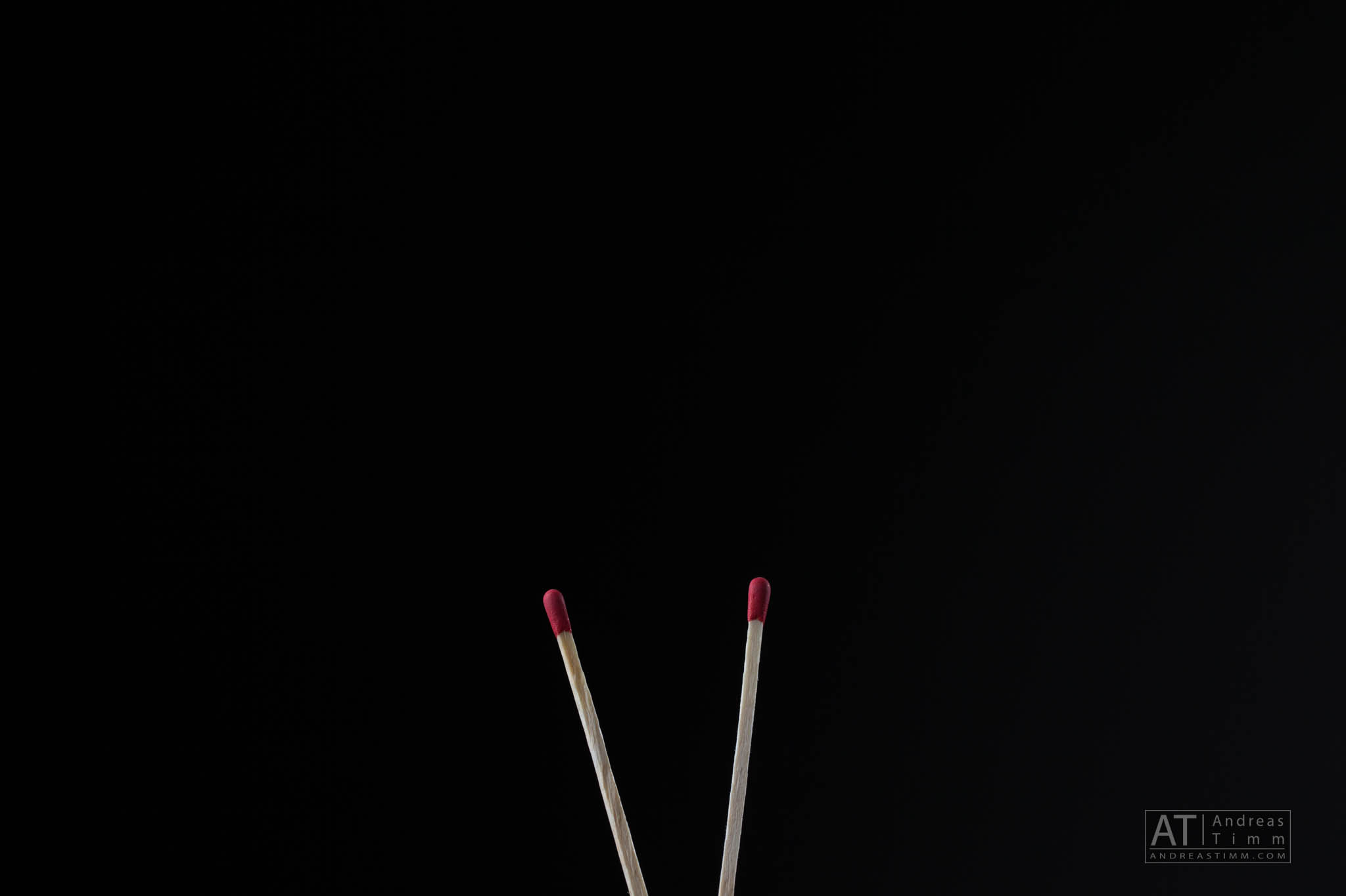 Two unlit matches with red tips on a black background.