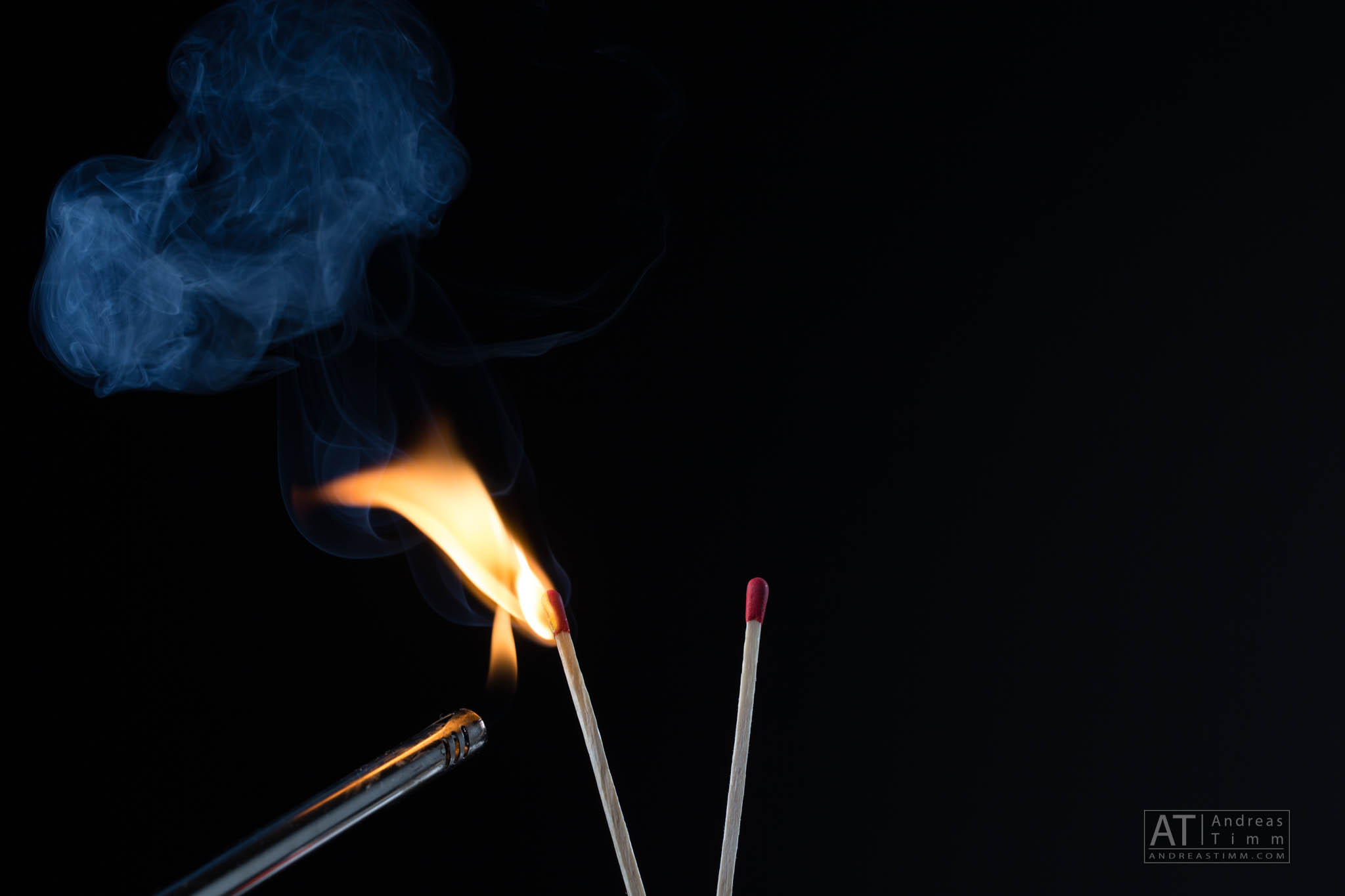 Lit matchstick with flame and smoke, next to an unlit match against a dark background.