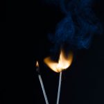 Two burning matches against a dark background with visible blue smoke curling upwards.