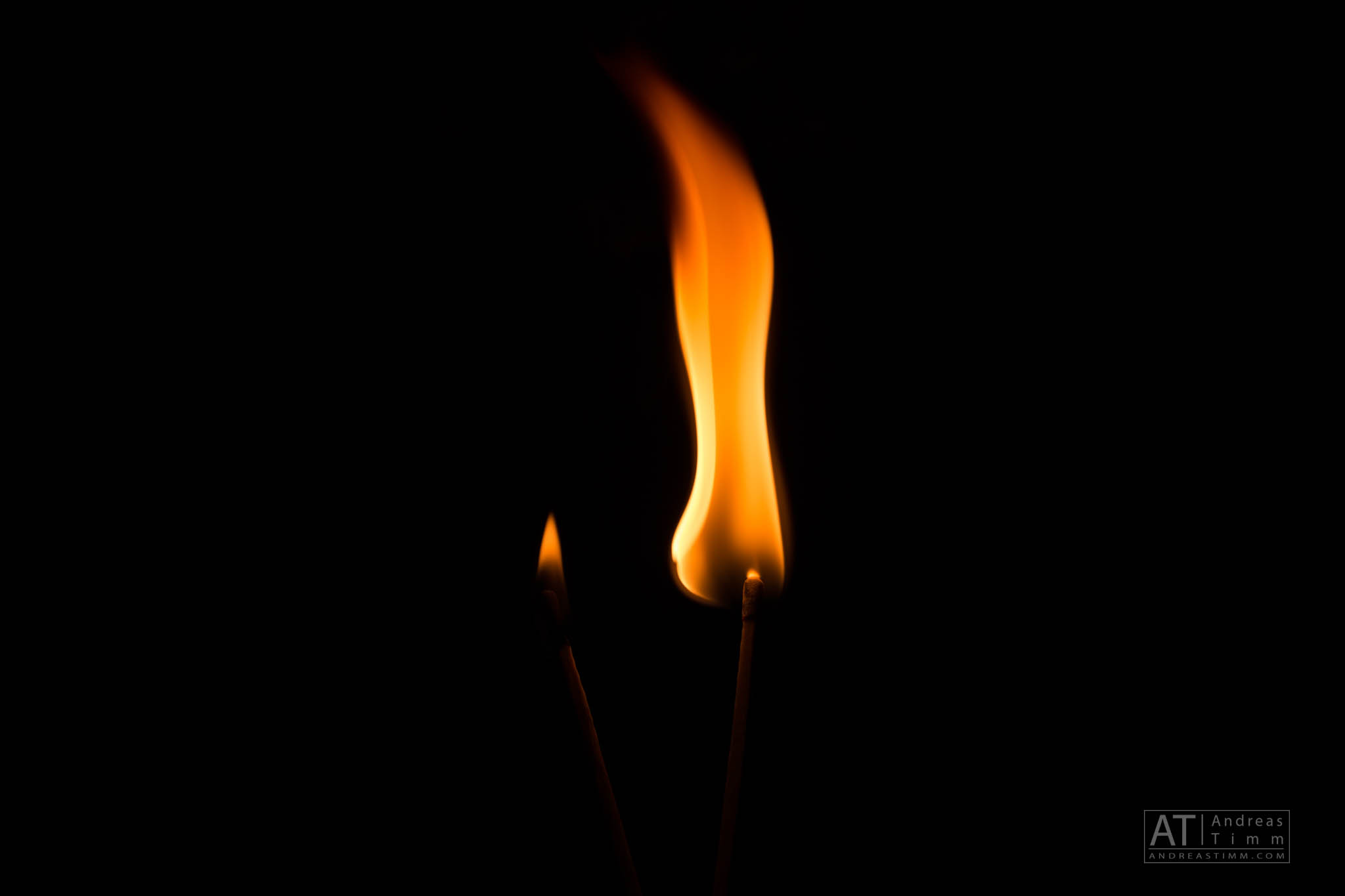 Two burning matches with bright orange flames against a dark background.