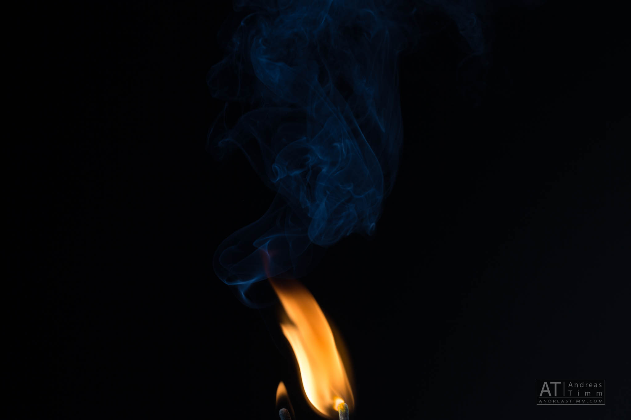 Orange flame with swirling blue smoke against a dark background.