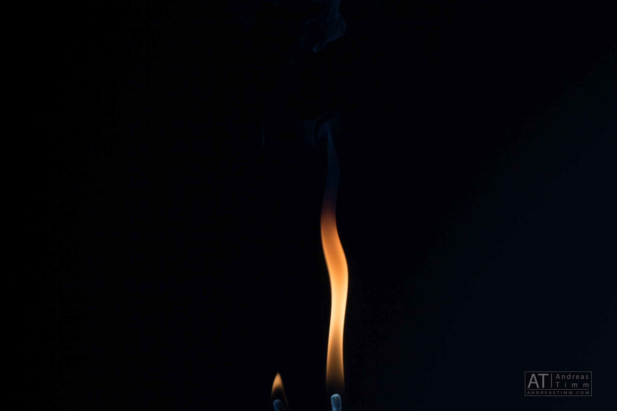 Lit match flame with dark background, emitting smoke, capturing glow and warmth.
