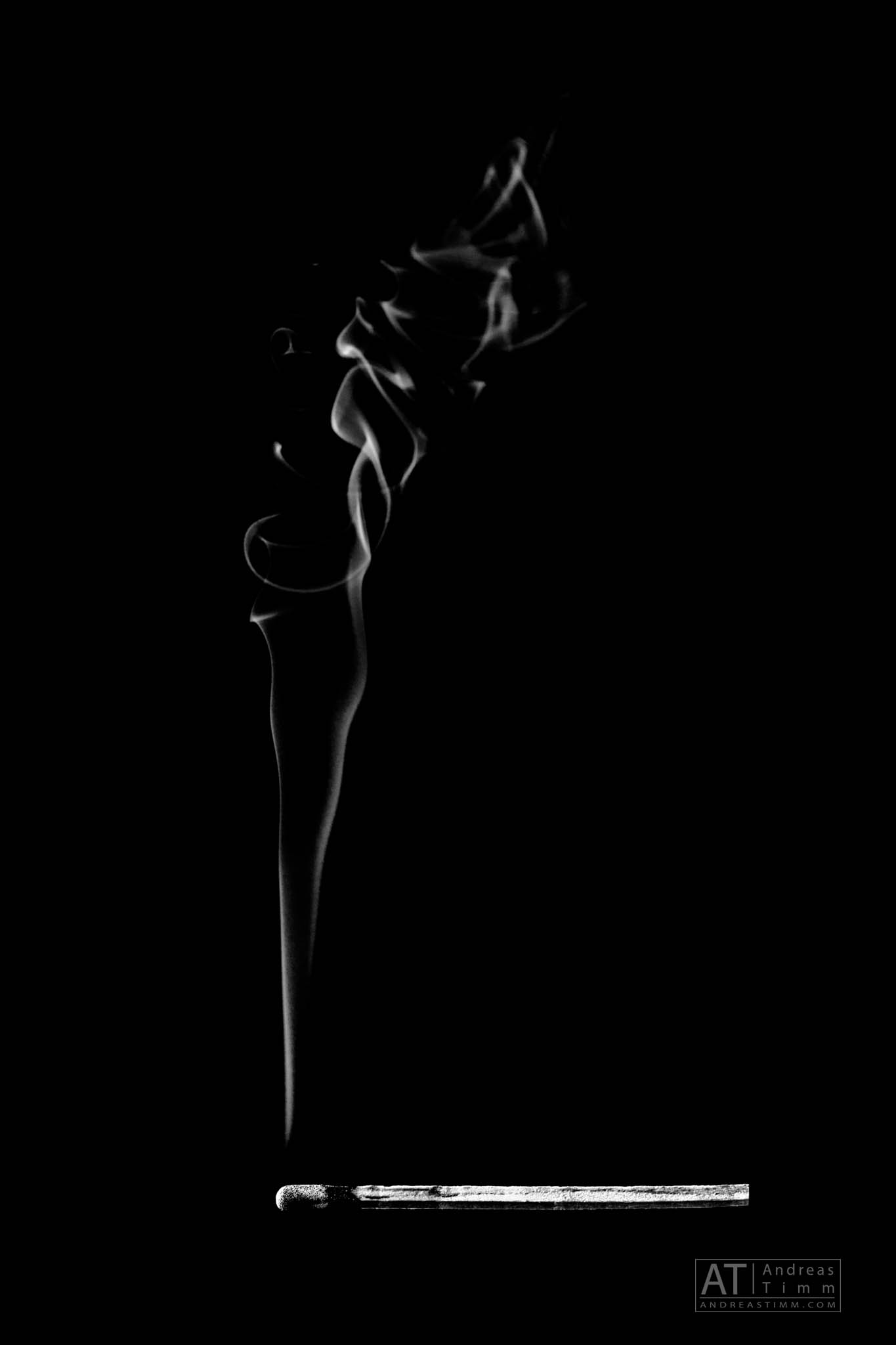 A matchstick on a dark background with a swirling plume of smoke rising above it.
