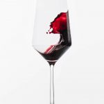 Red wine splashing in a clear wine glass against a white background.