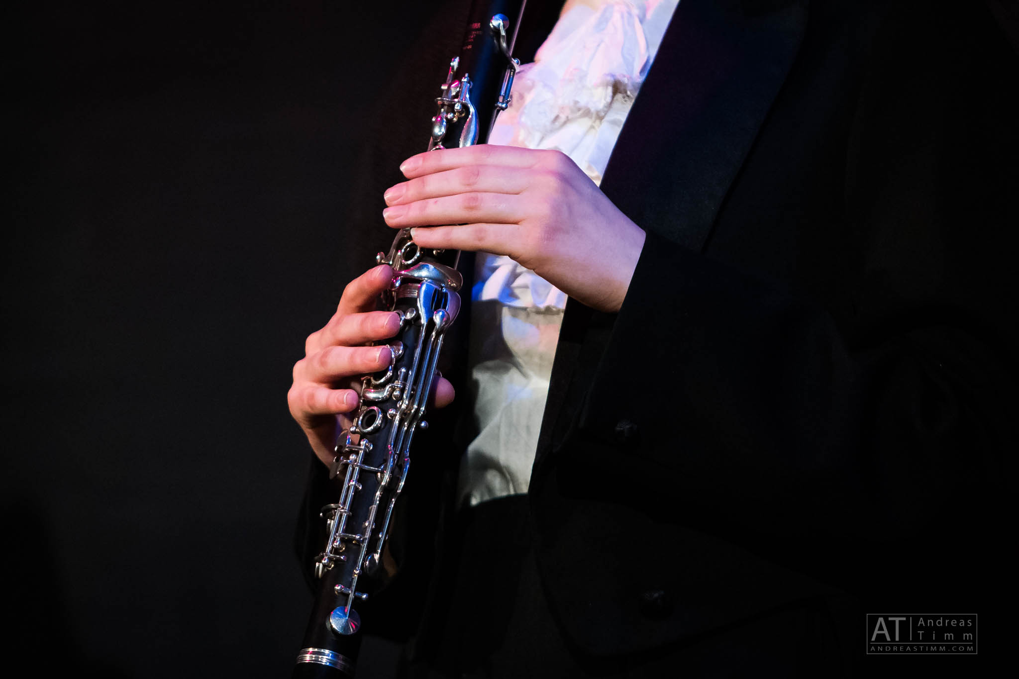 Person playing a clarinet in formal attire, hands focused on the instrument.