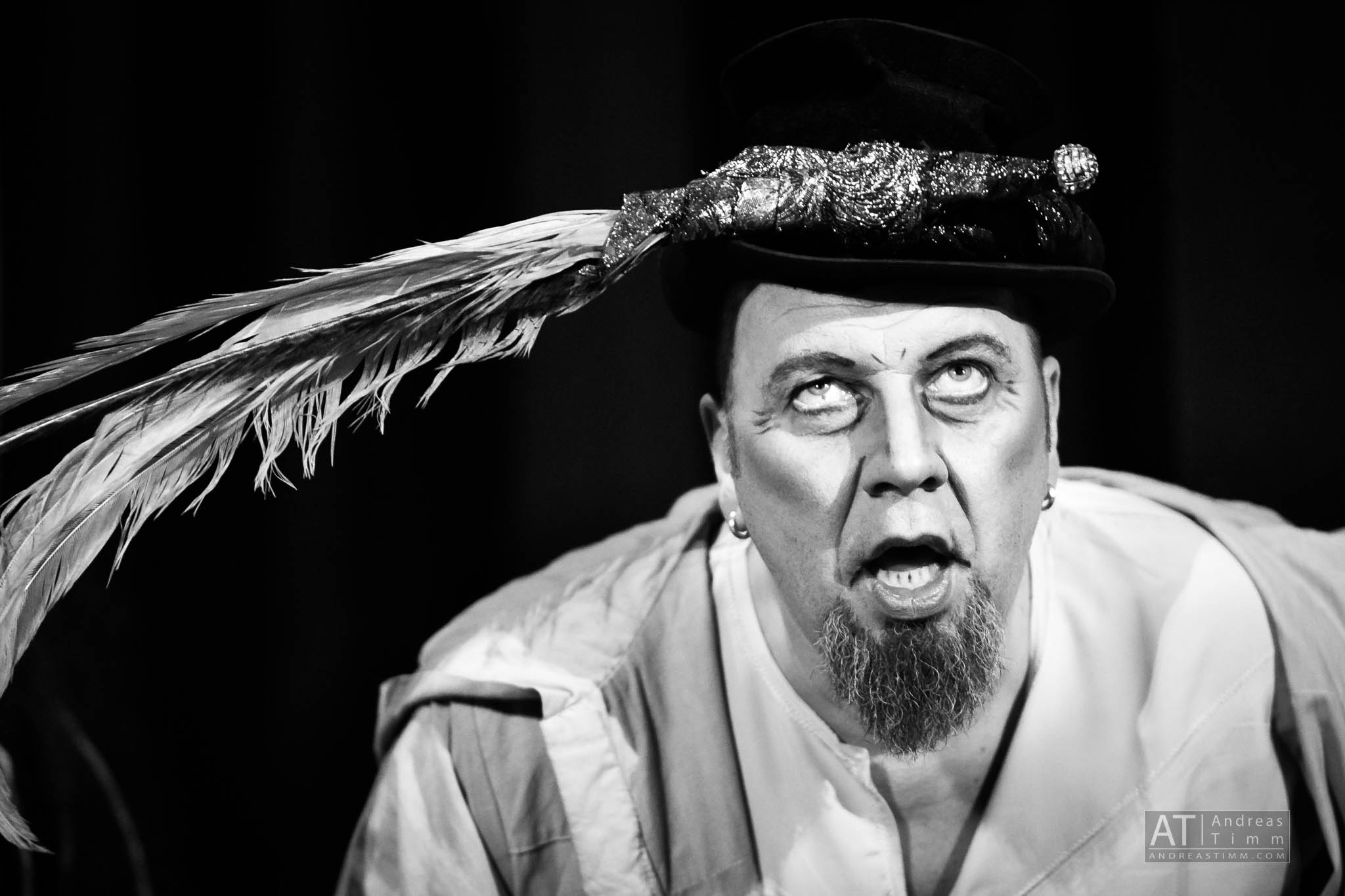 Black and white portrait of an expressive actor with a feathered hat, performing on stage.