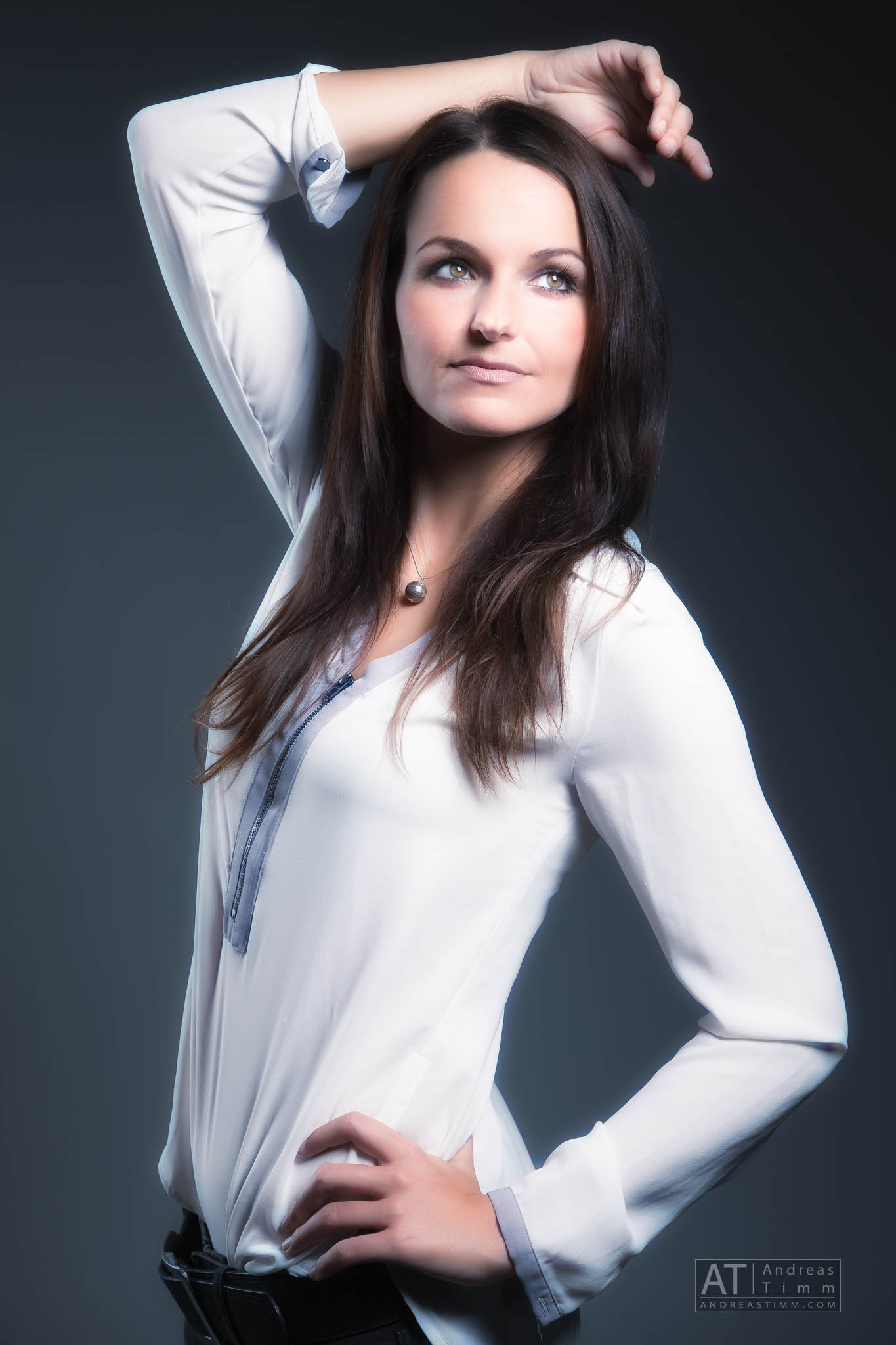Woman in a white blouse posing against a dark background, with one arm raised above her head.