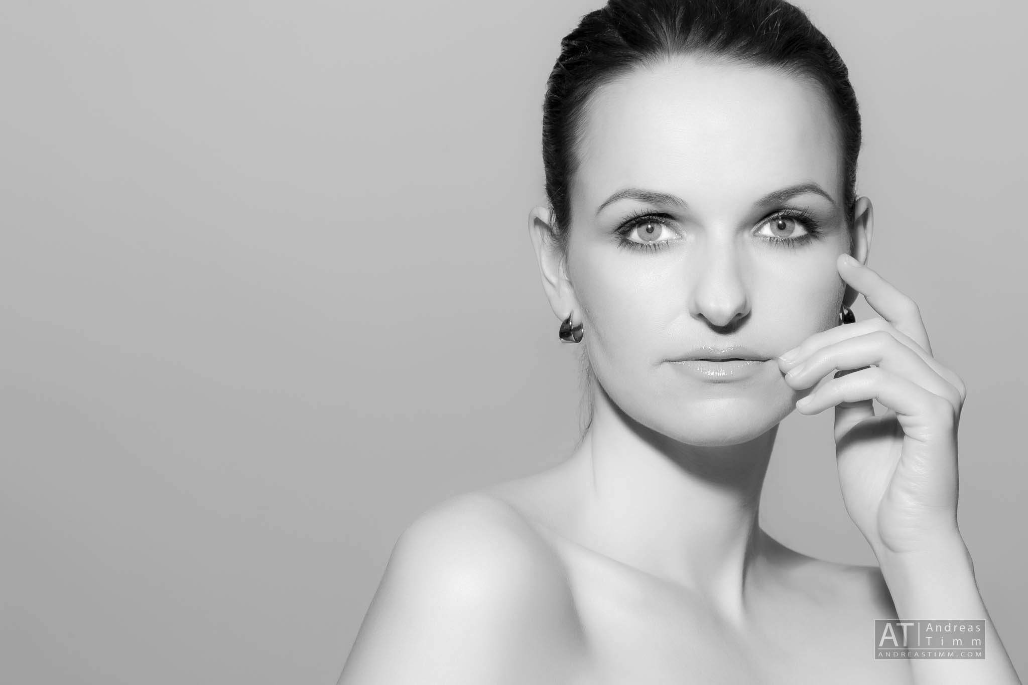 Black and white portrait of a woman with short hair, wearing earrings, touching her face.