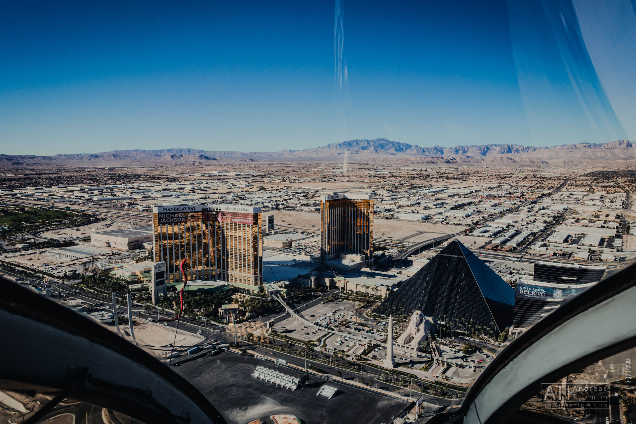 Aerial view of Las Vegas showing Mandalay Bay and Luxor Hotel against a backdrop of desert and mountains.