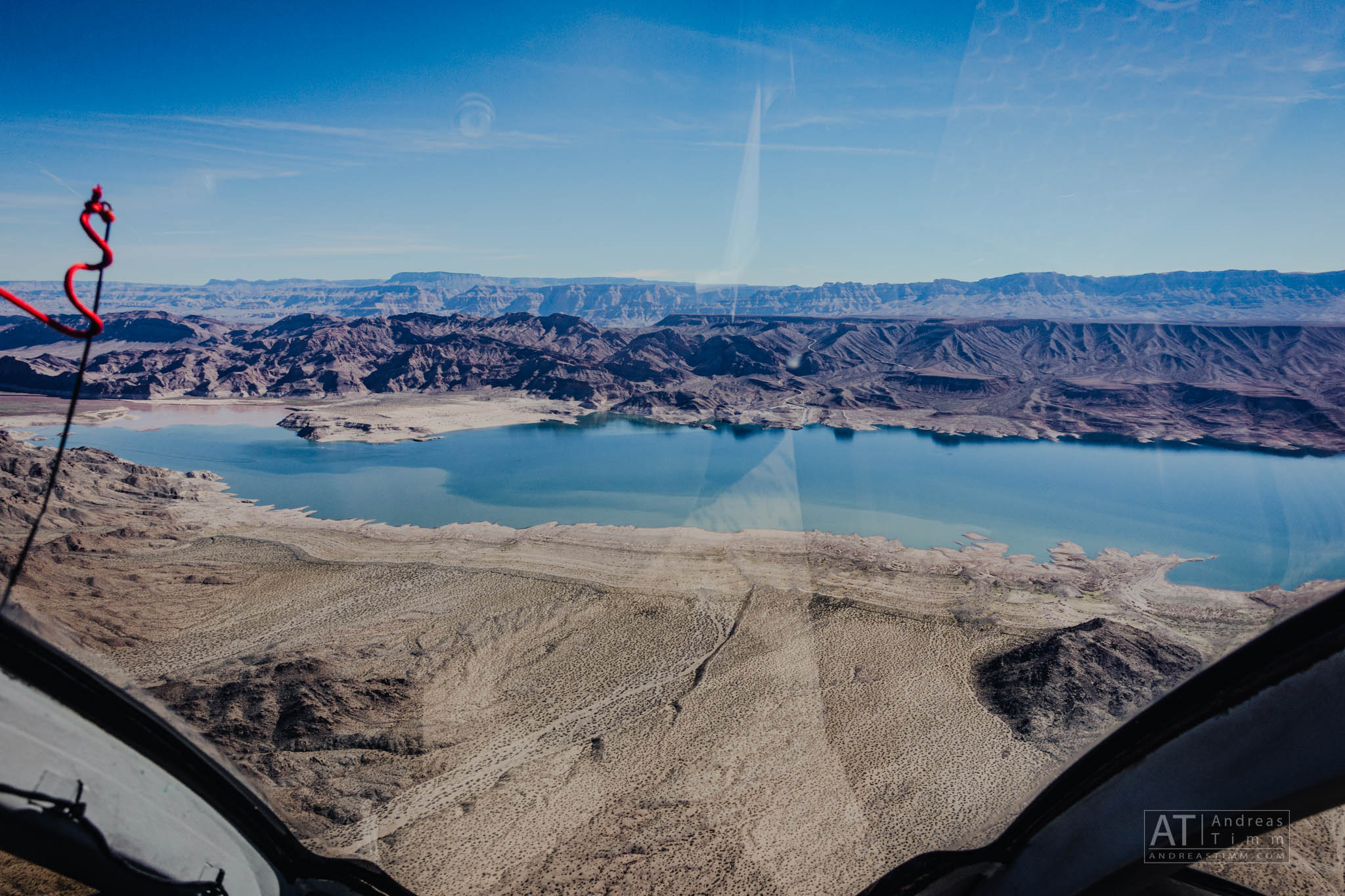 Aerial view of mountains and serene lake from a helicopter cockpit on a clear day.