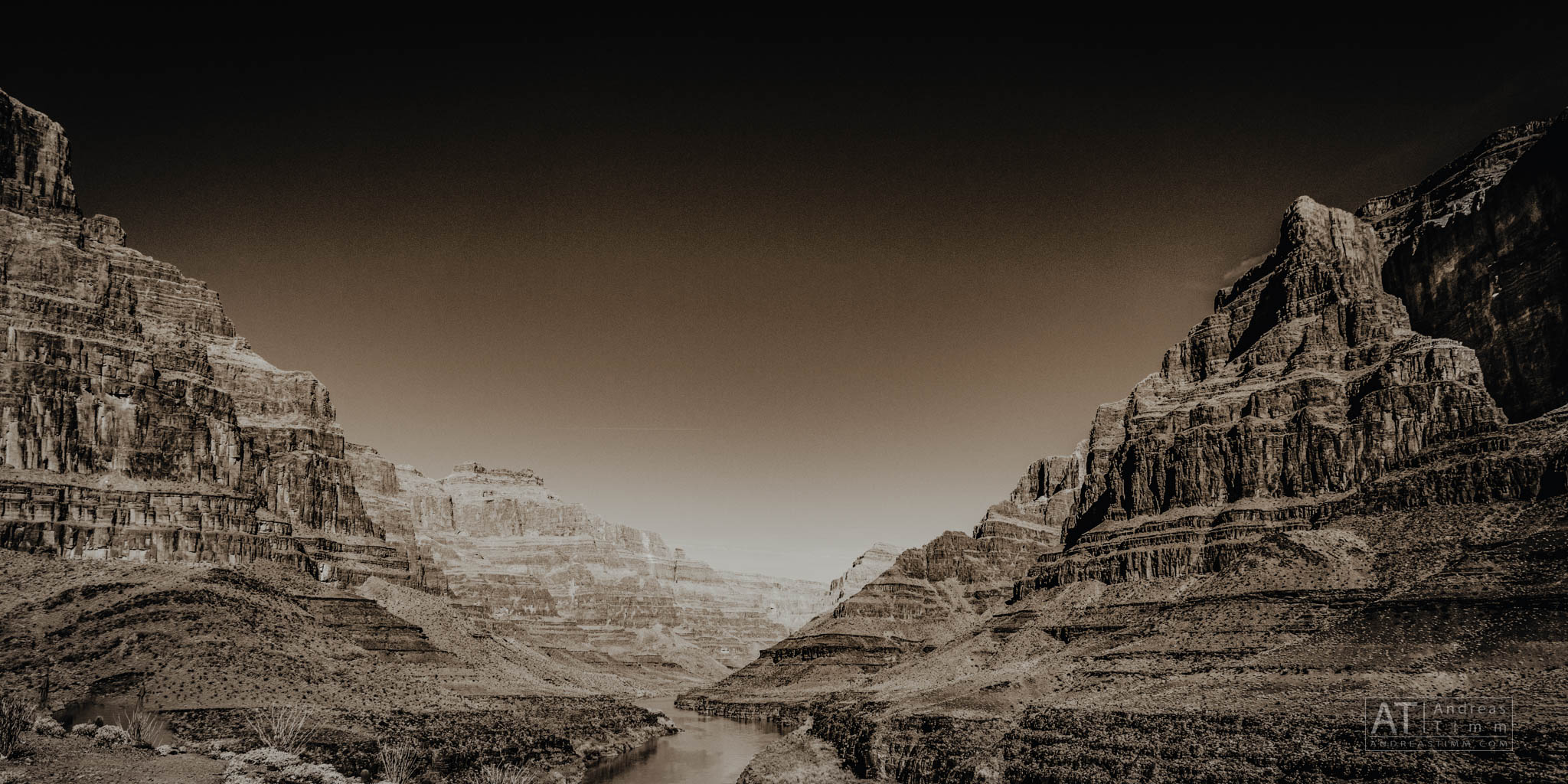 Sepia-toned photograph of a rugged canyon landscape with a river flowing between towering rock formations.