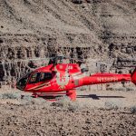 Red helicopter on rocky terrain with steep canyon background.
