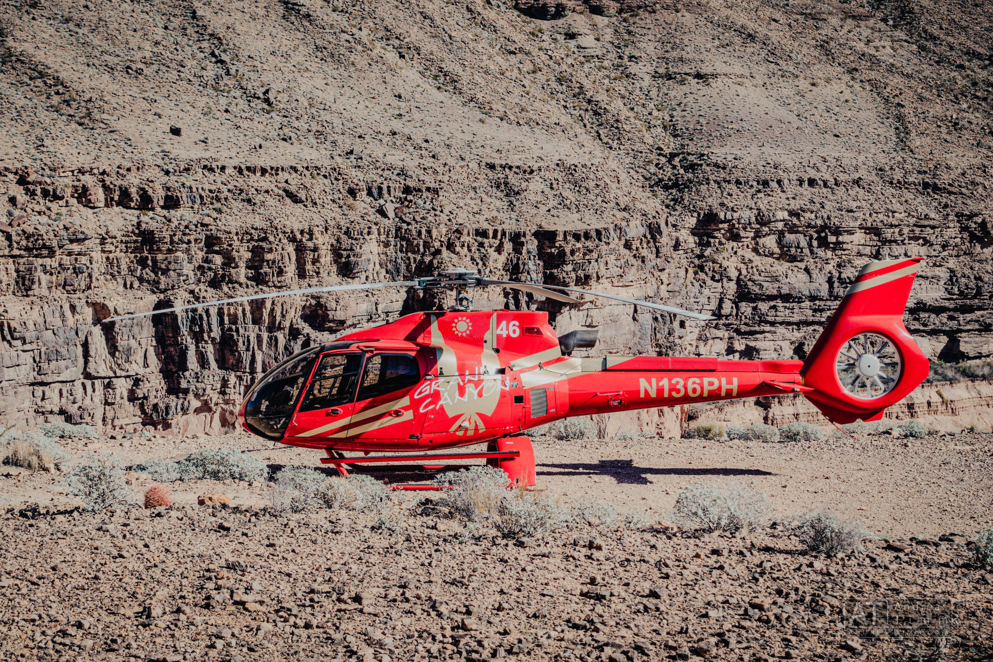 Red helicopter on rocky terrain with steep canyon background.
