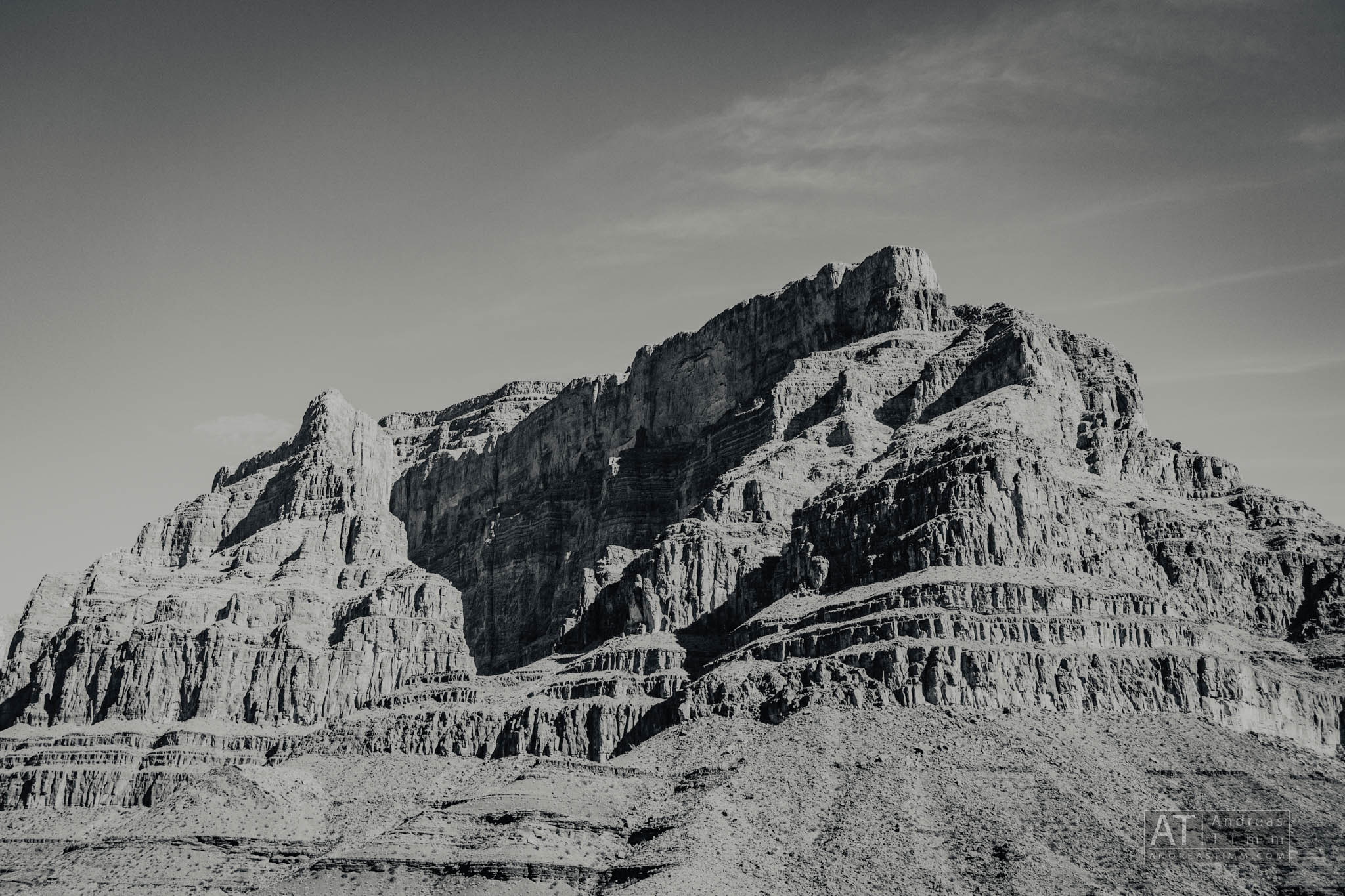 Black and white photo of a rugged, layered rock mountain under a clear sky.