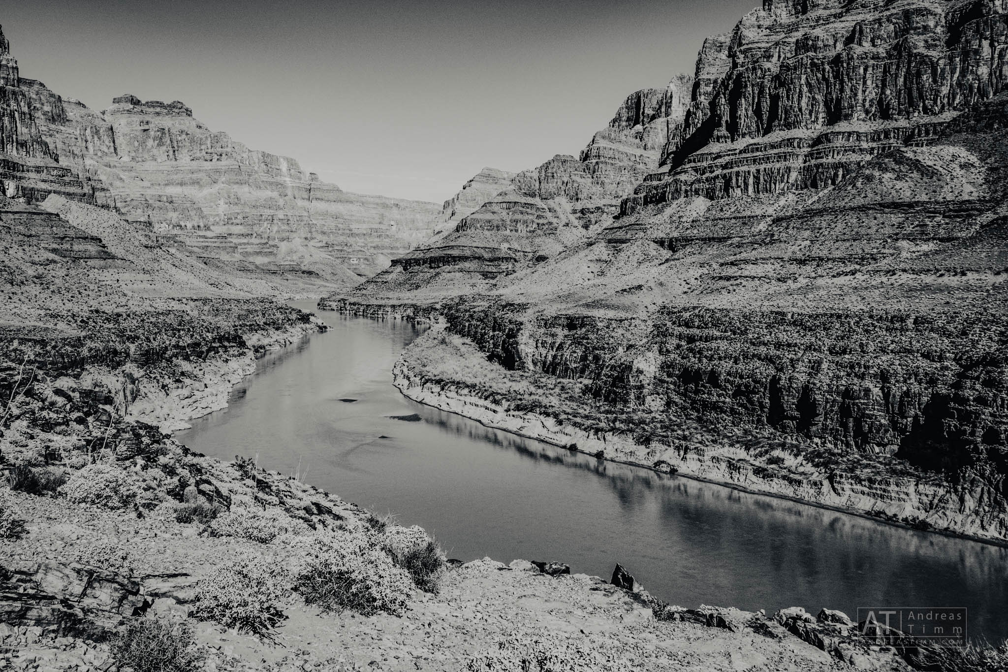 Black and white view of a river winding through the rugged Grand Canyon, surrounded by steep rocky cliffs.