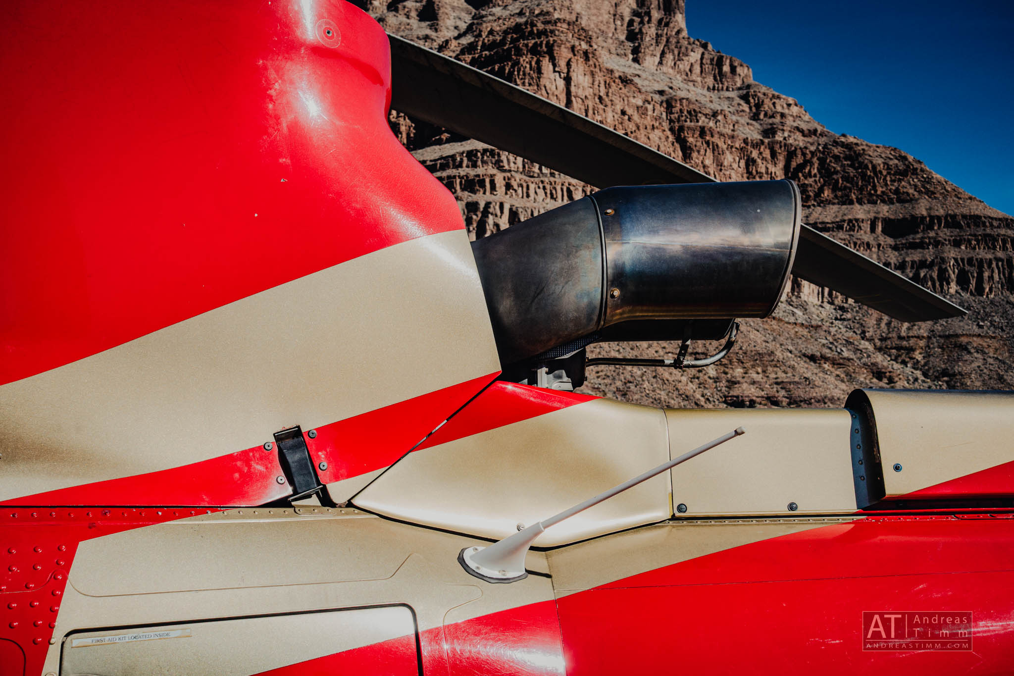 Close-up of a red helicopter tail with mountains in the background under a clear blue sky.