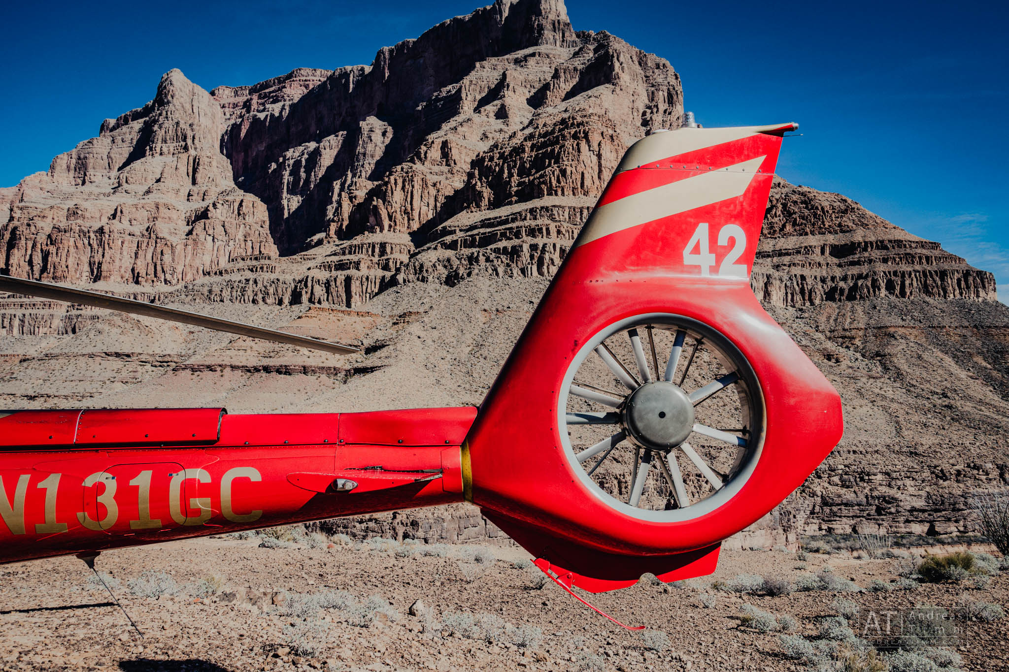 Red helicopter tail near Grand Canyon rock formations under clear blue sky.