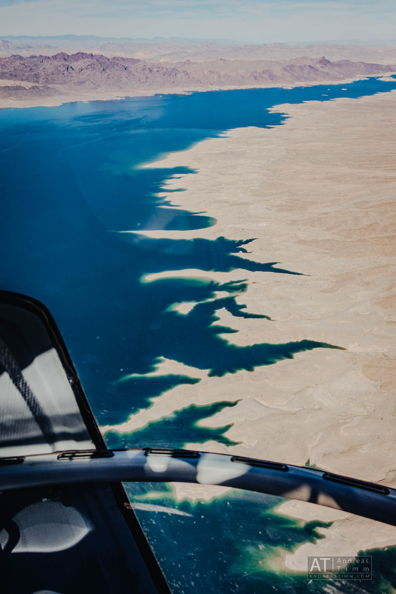 Aerial view of a vast desert coastline with jagged edges meeting a deep blue sea under a clear sky.