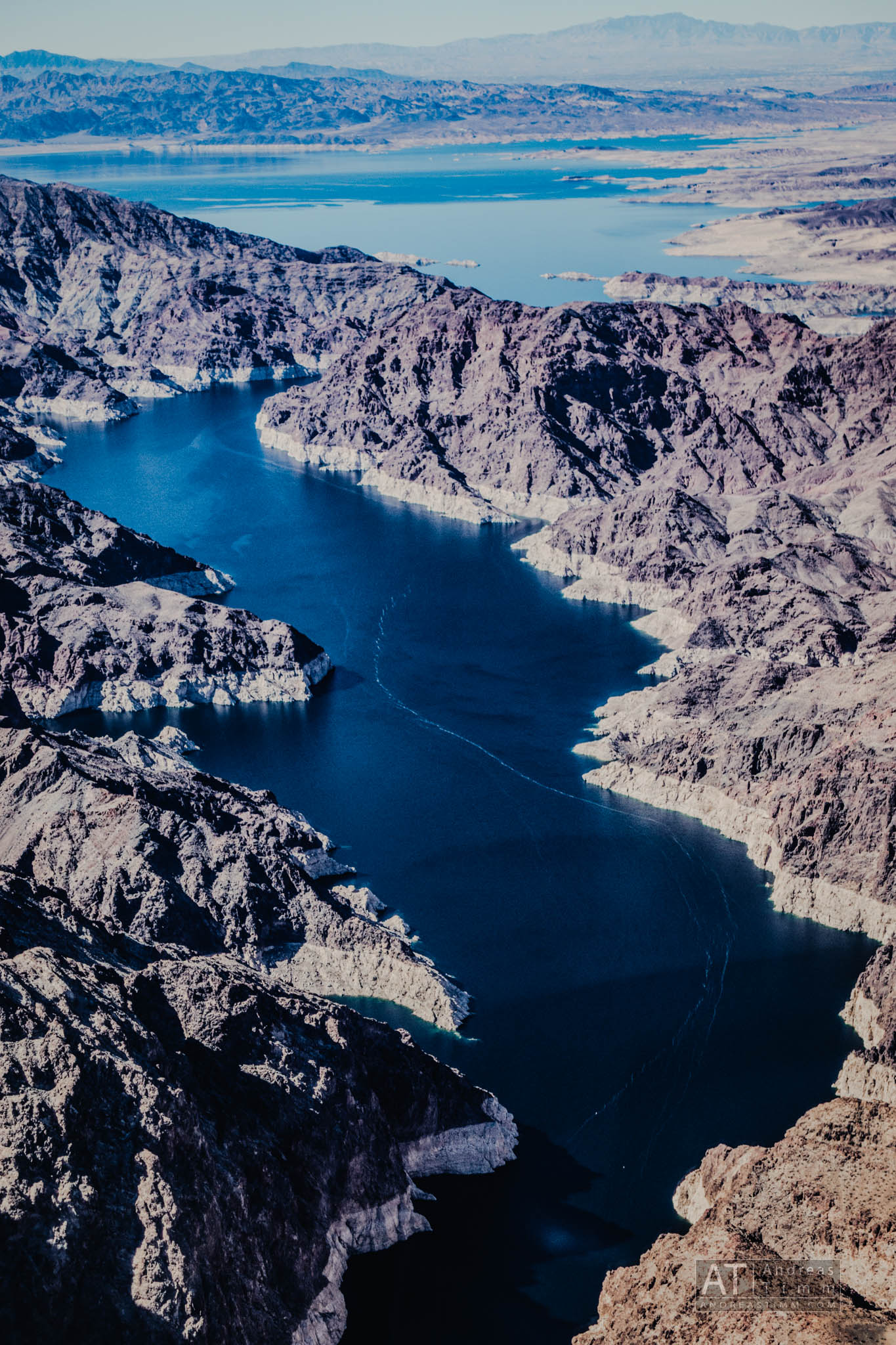 Aerial view of expansive blue lake surrounded by rugged desert mountains under a clear sky.