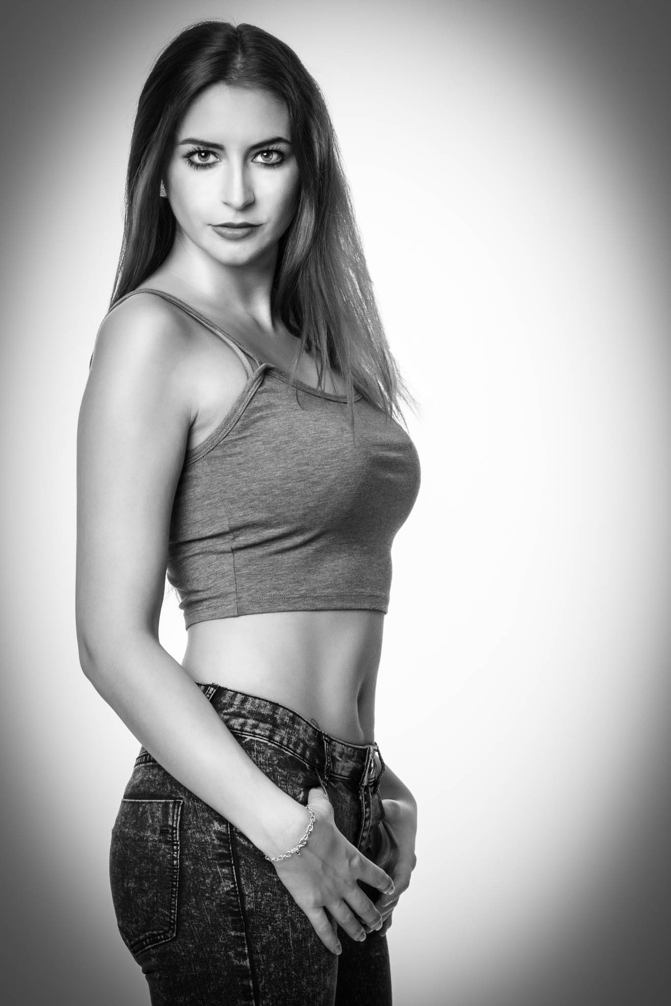 Black and white portrait of a woman in a grey crop top and jeans, looking confidently at the camera.
