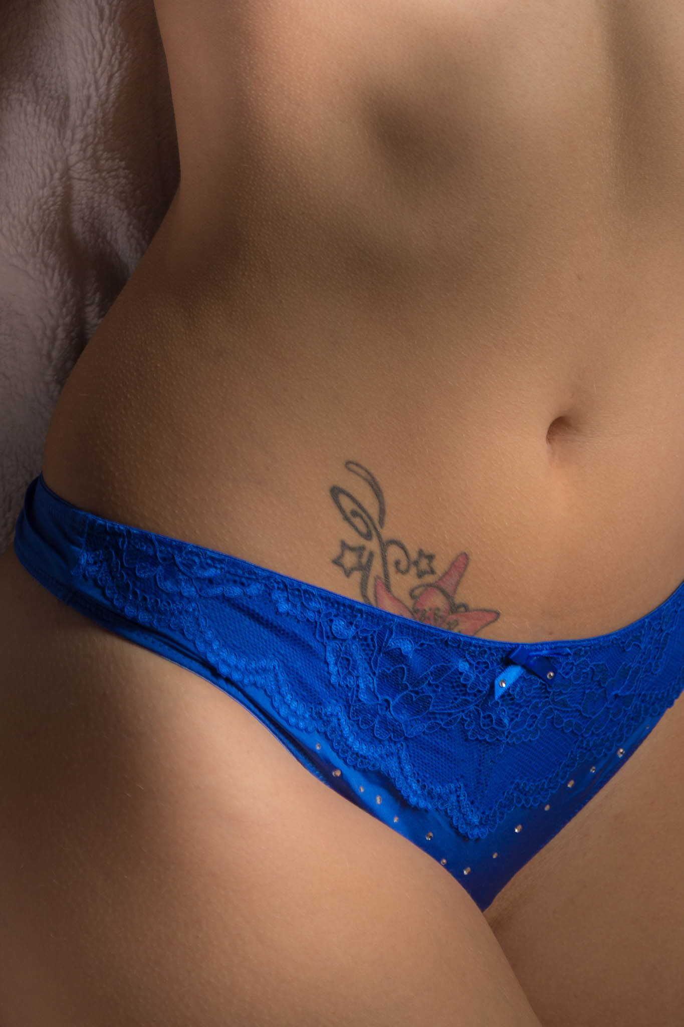 Close-up of a woman’s waist with a floral tattoo wearing blue lace underwear.