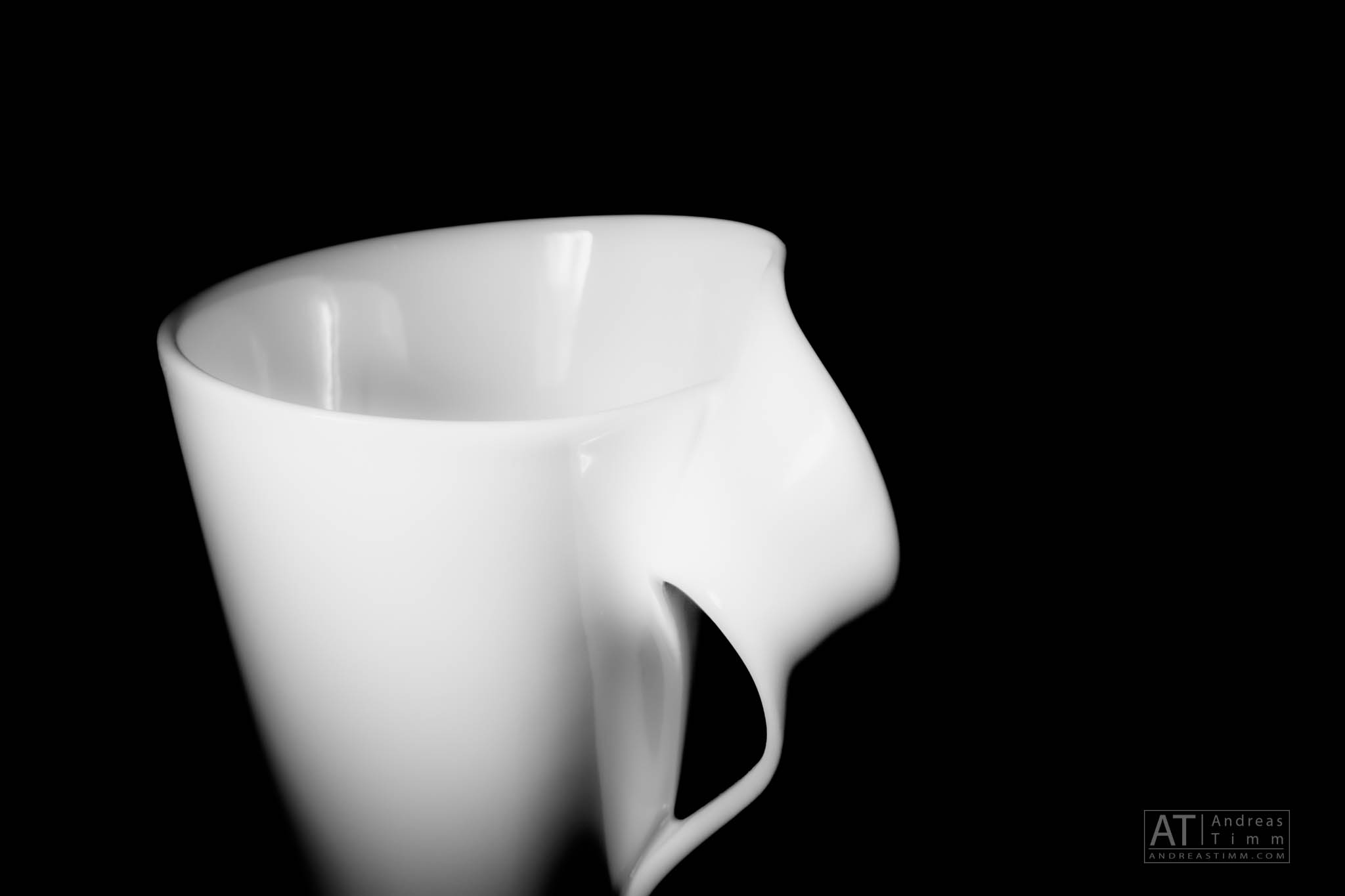 White ceramic mug with unique, artistic handle on black background.