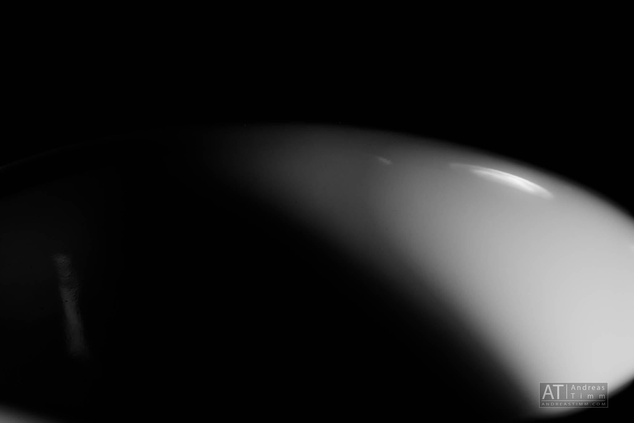 Abstract close-up of a white curved surface against a black background, showcasing light and shadow interplay.