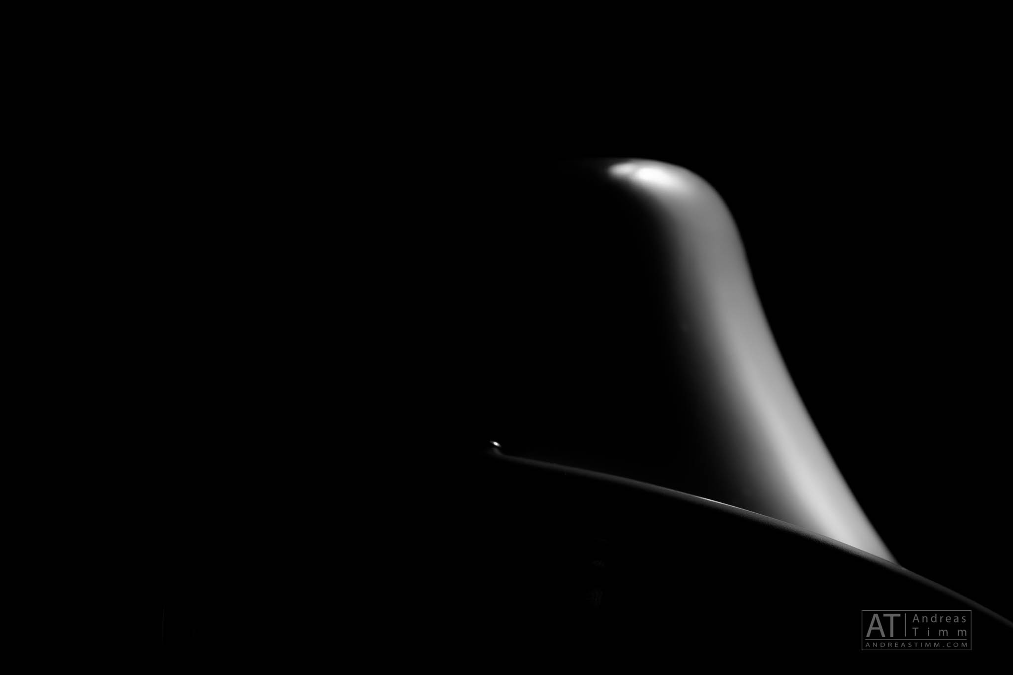 Abstract black and white image of a curved, smooth surface in shadows against a dark background.