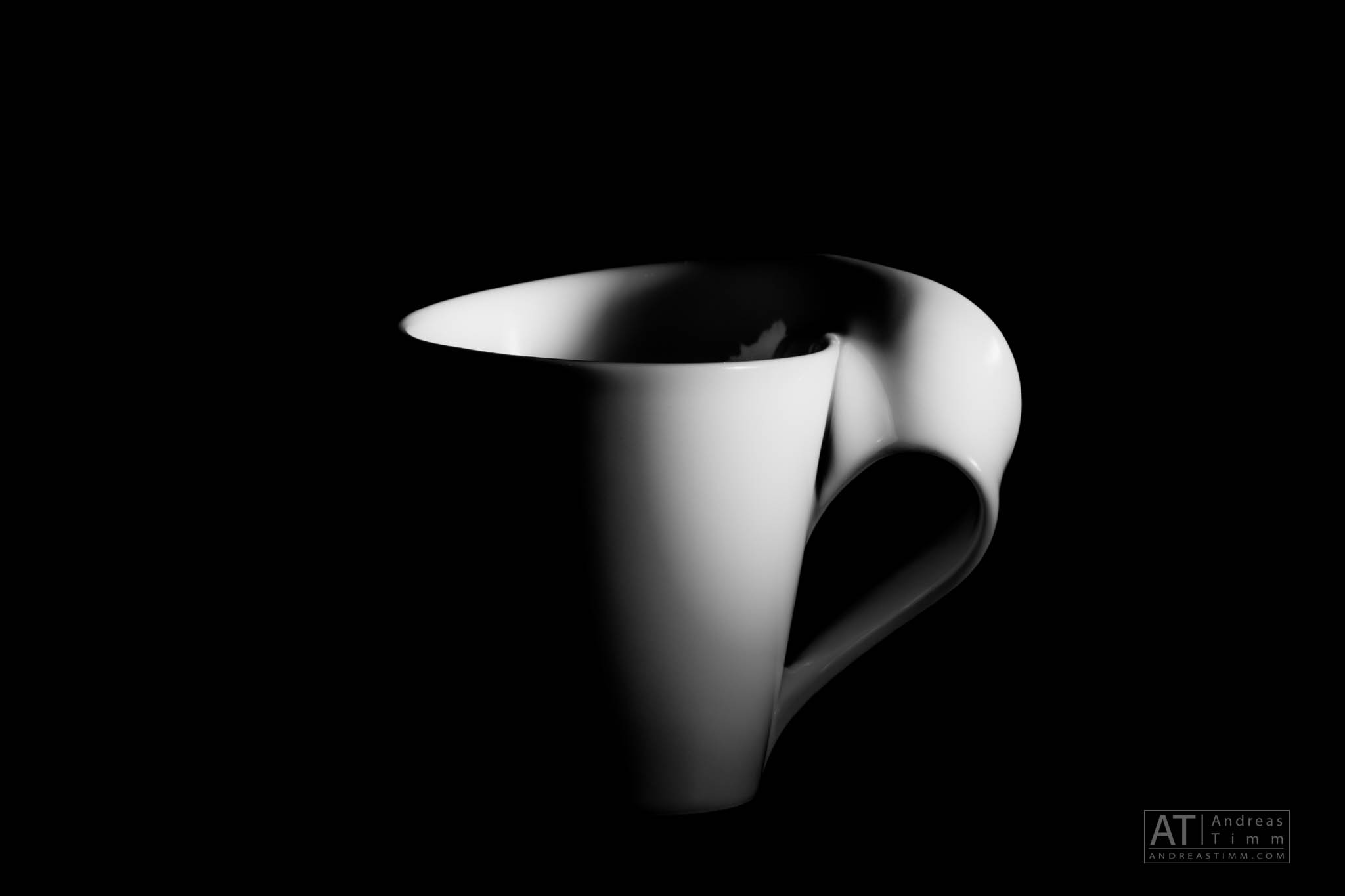 Stylish white mug with an artistic handle in dramatic lighting against a black background.