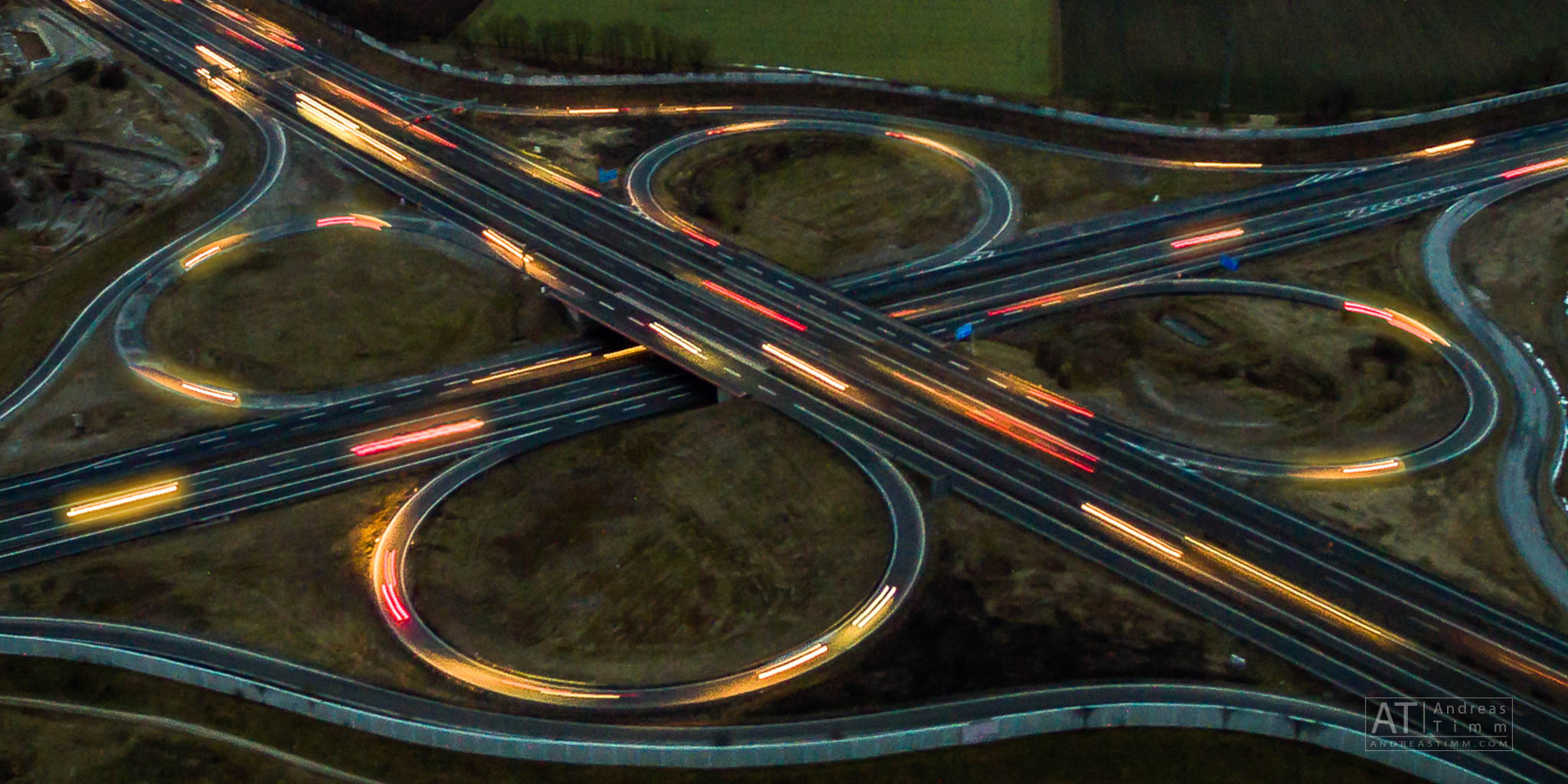 Aerial view of illuminated cloverleaf interchange with moving cars at dusk, showcasing highway infrastructure design.