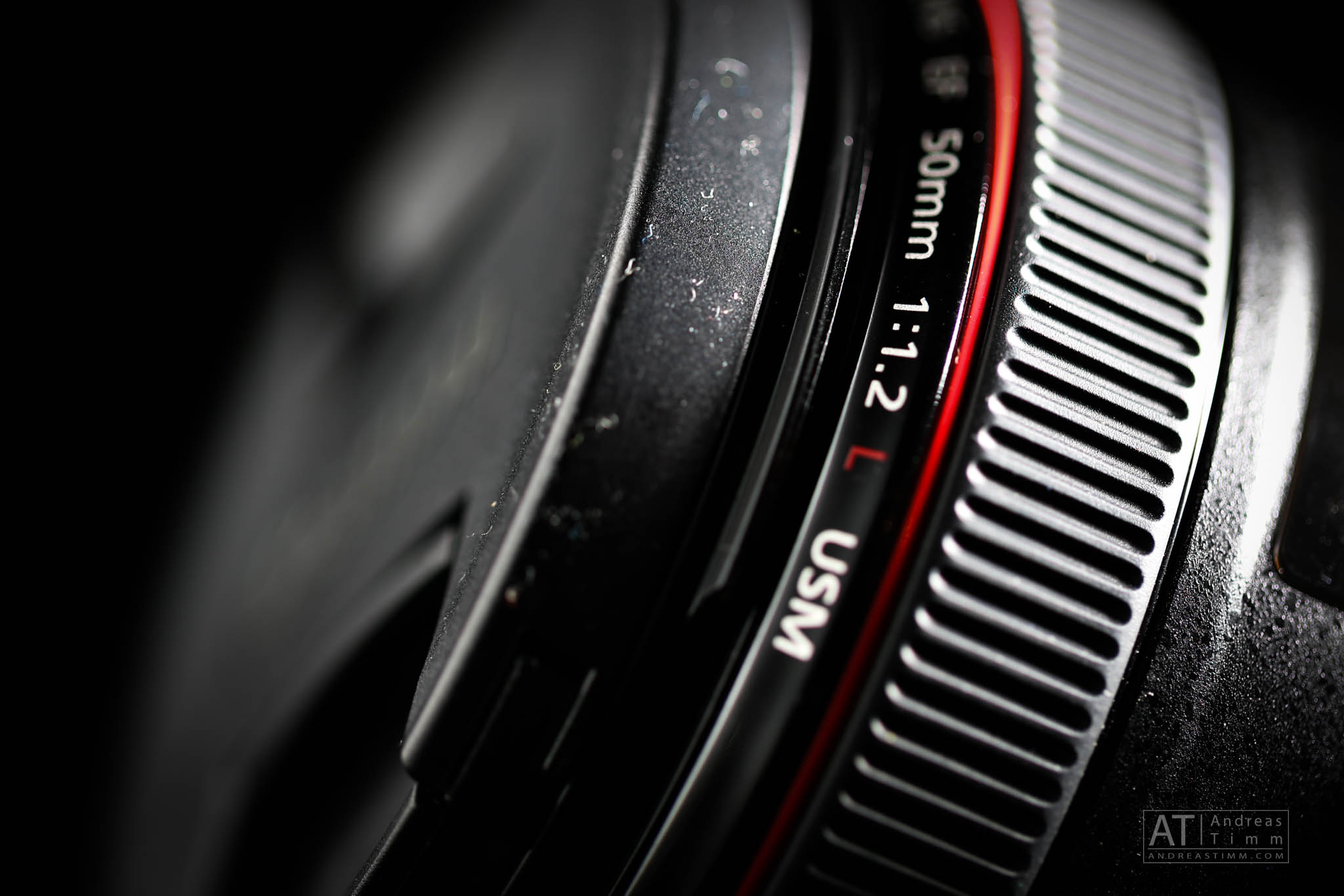 Close-up of a 50mm f/1.2 L USM camera lens with focus on textured ring and red accent line, set against a dark background.