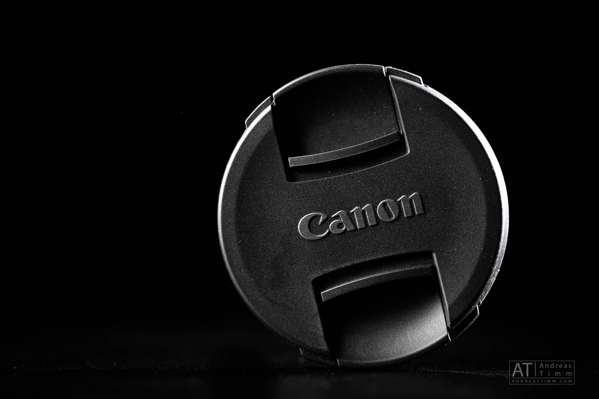 Close-up of a black Canon lens cap against a dark background.