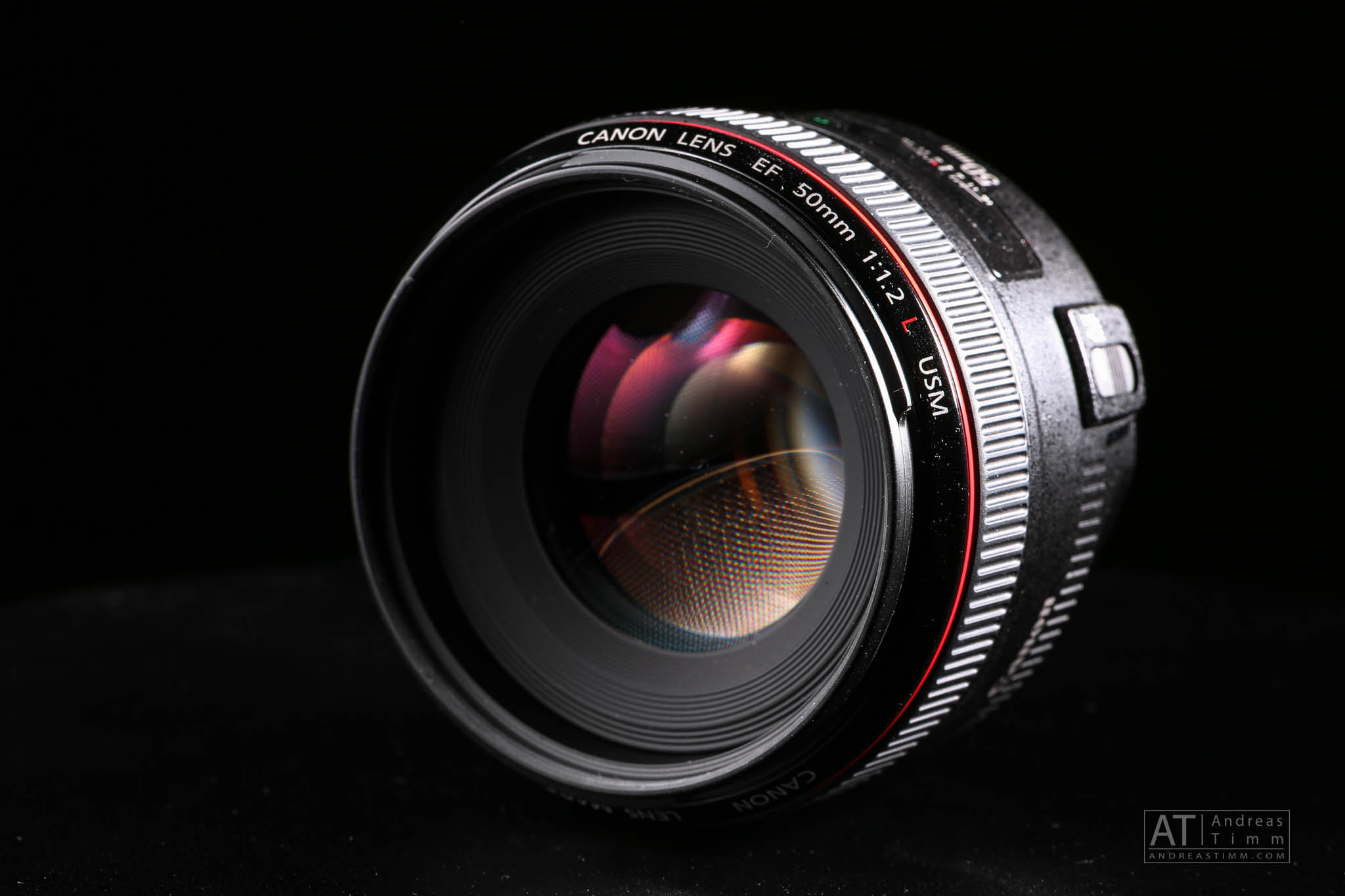 Close-up of Canon 50mm f/1.2 L lens with reflections, set against a black background.