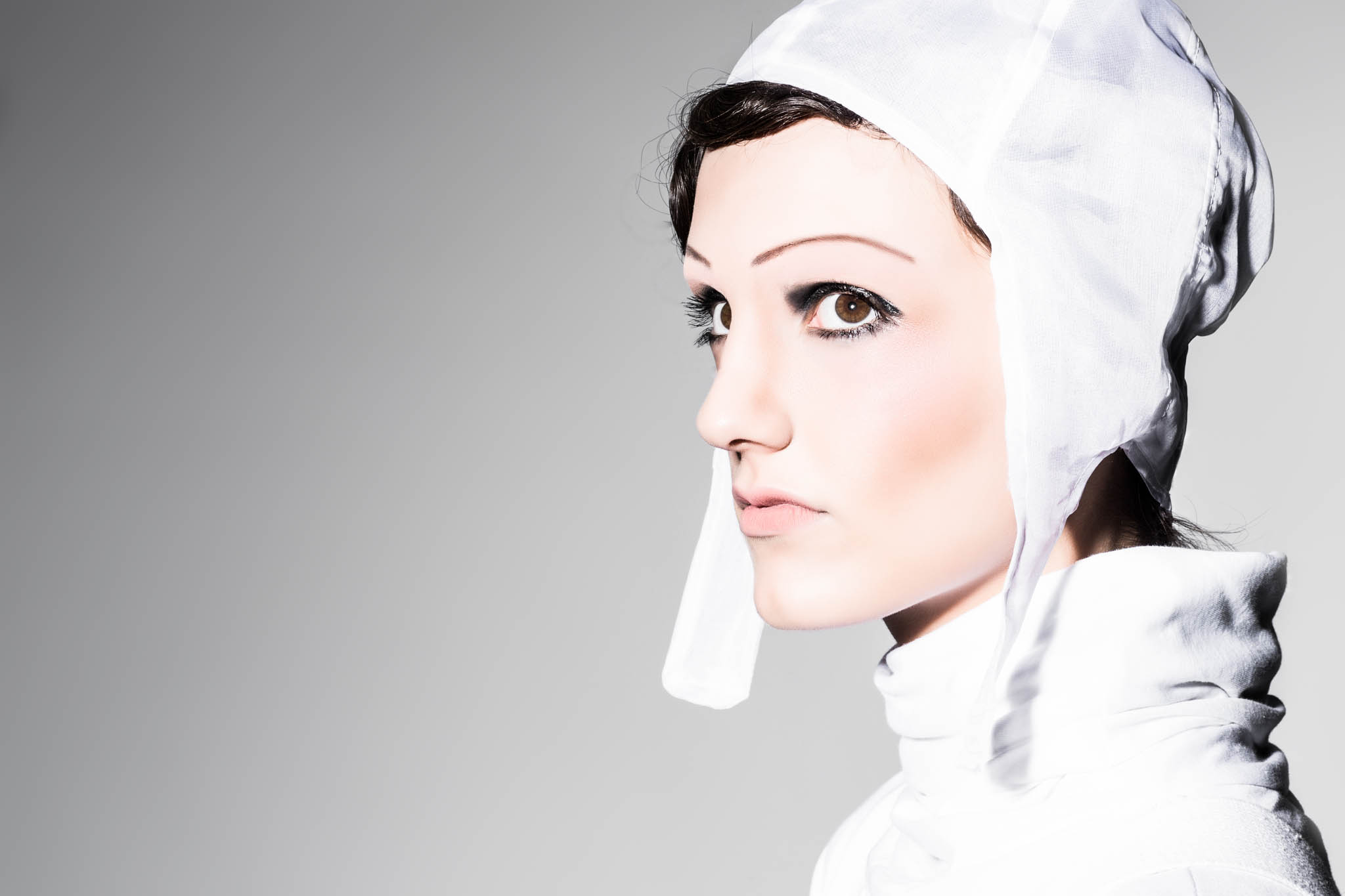 Profile of woman in white headscarf and high-collared outfit against gray gradient background.