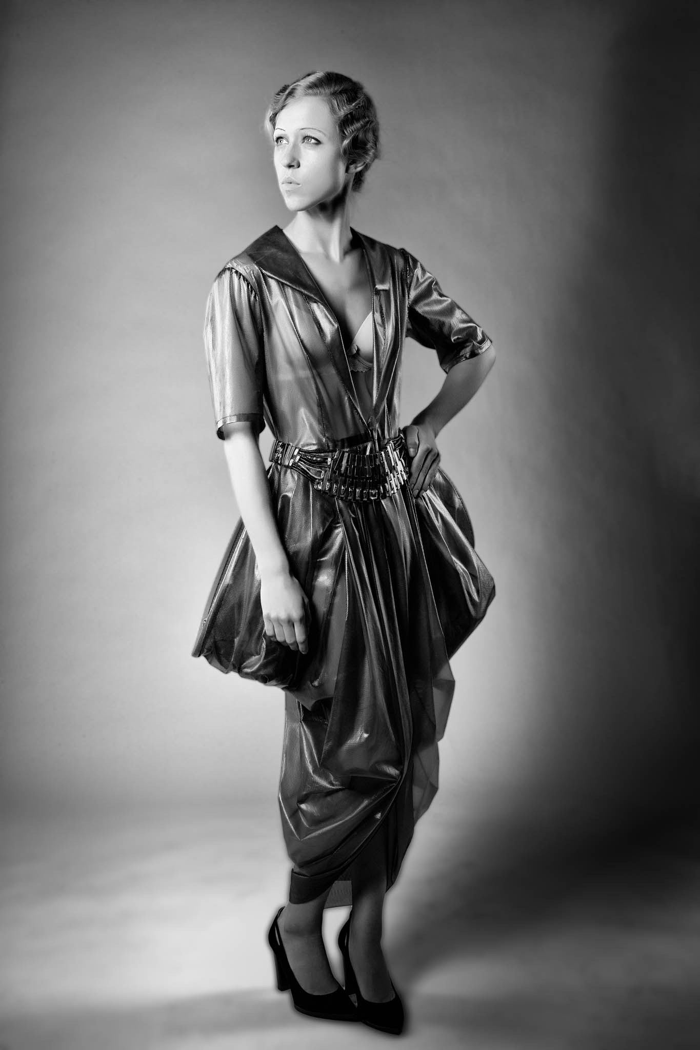 Black and white photo of a woman in a shiny dress with retro hairstyle, posing stylishly in high heels.