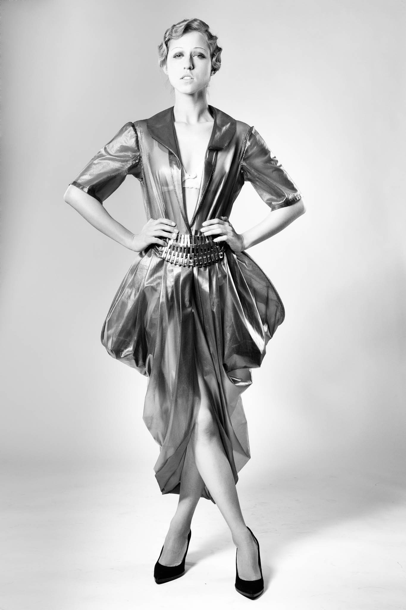 Fashion model in a shiny metallic dress and high heels, hands on hips, posing confidently in a studio.